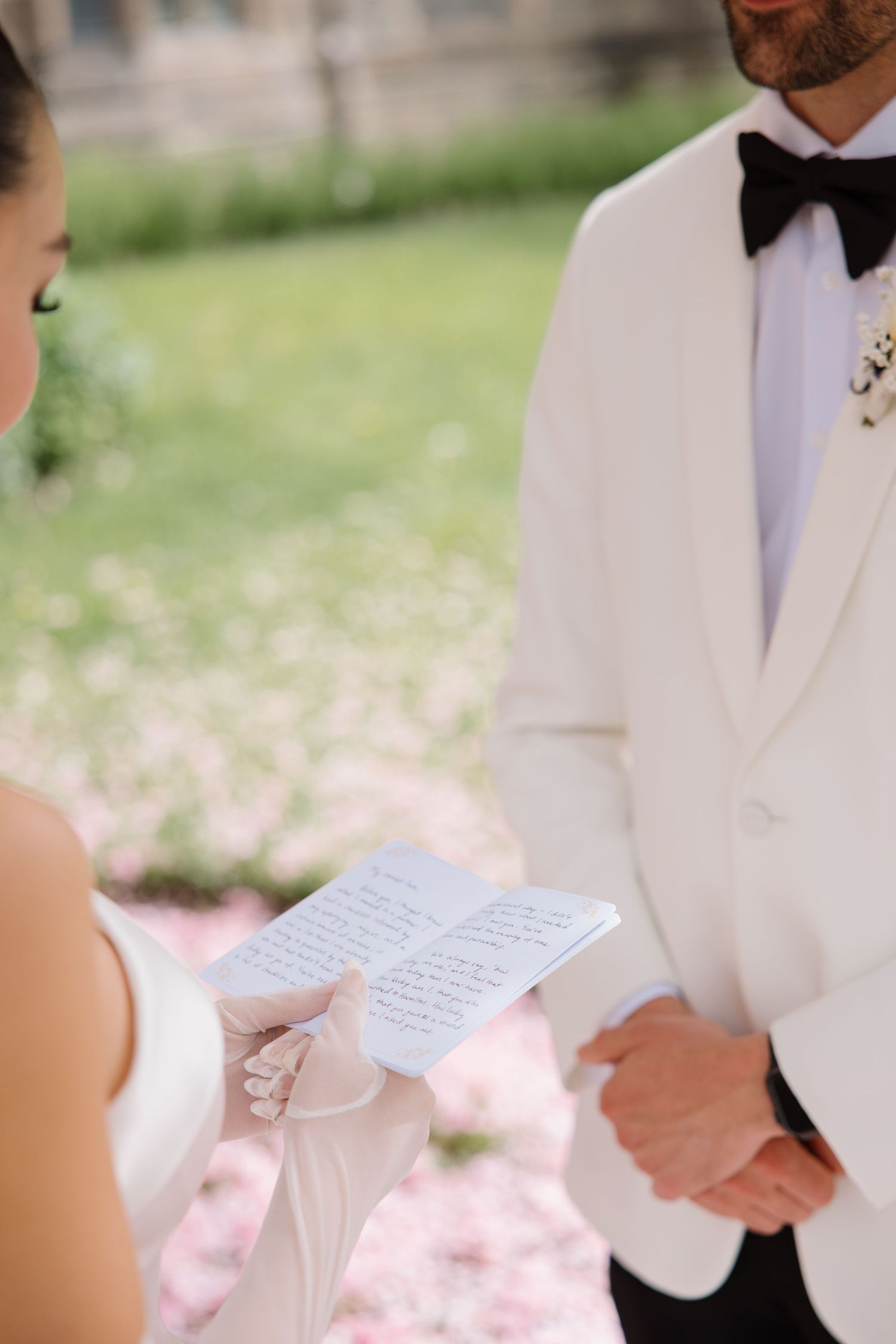 Couple at wedding ceremony exchanging handwritten vows with groom in white tuxedo jacket and black bow tie.