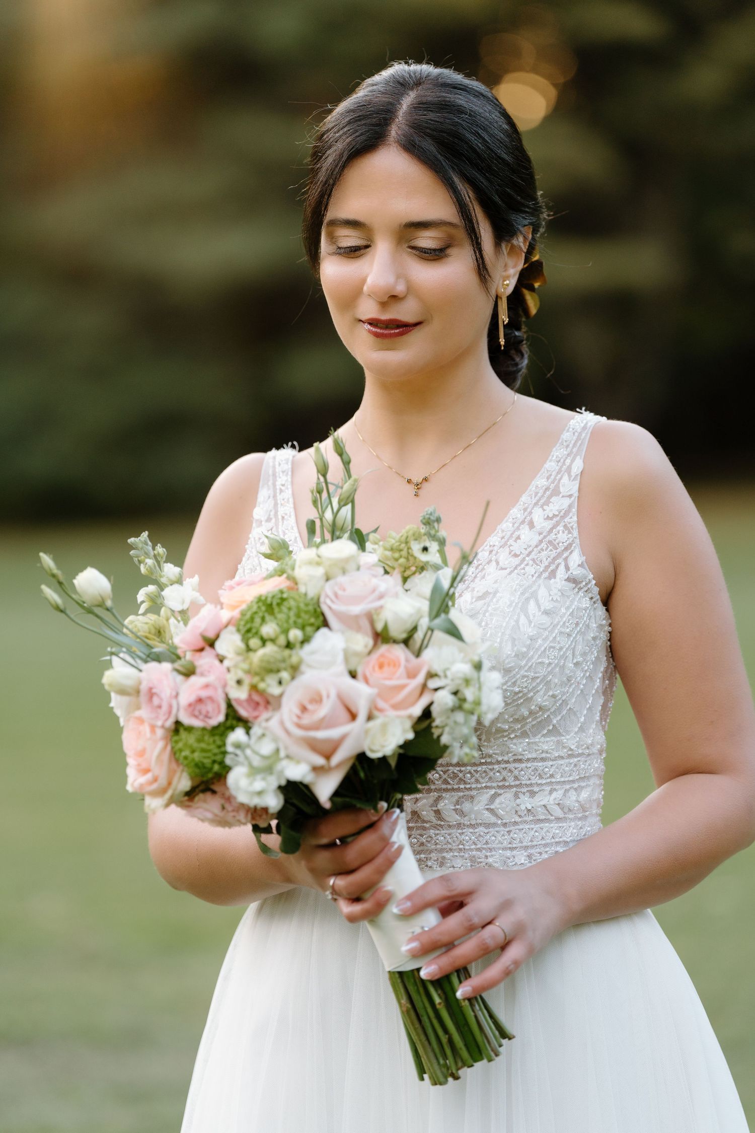 Bride in lace dress holding pink and white rose bouquet in golden afternoon light.