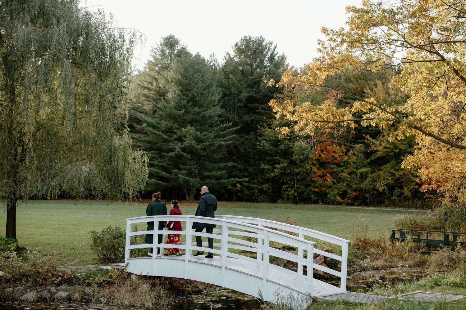 People standing on a white bridge surrounded by colorful fall foliage.