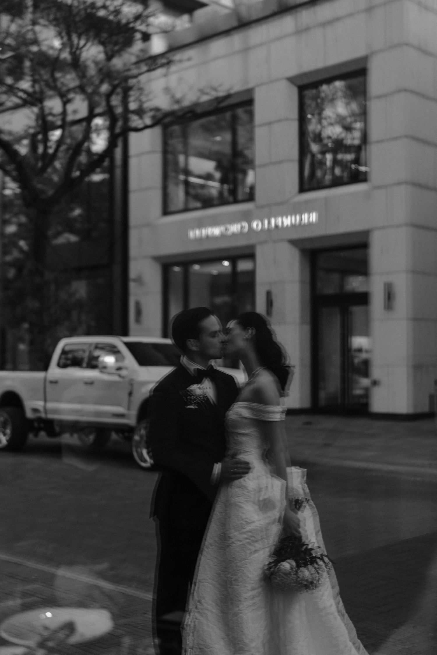 A black and white photograph of a couple dancing together on a city street in front of a building.