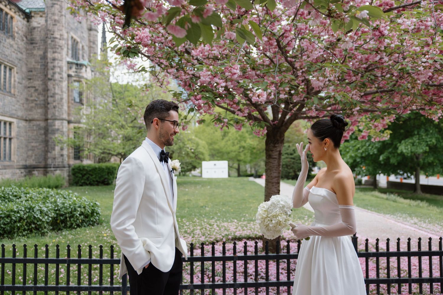 A romantic spring wedding scene with a couple standing under blooming cherry blossoms near a historic building.