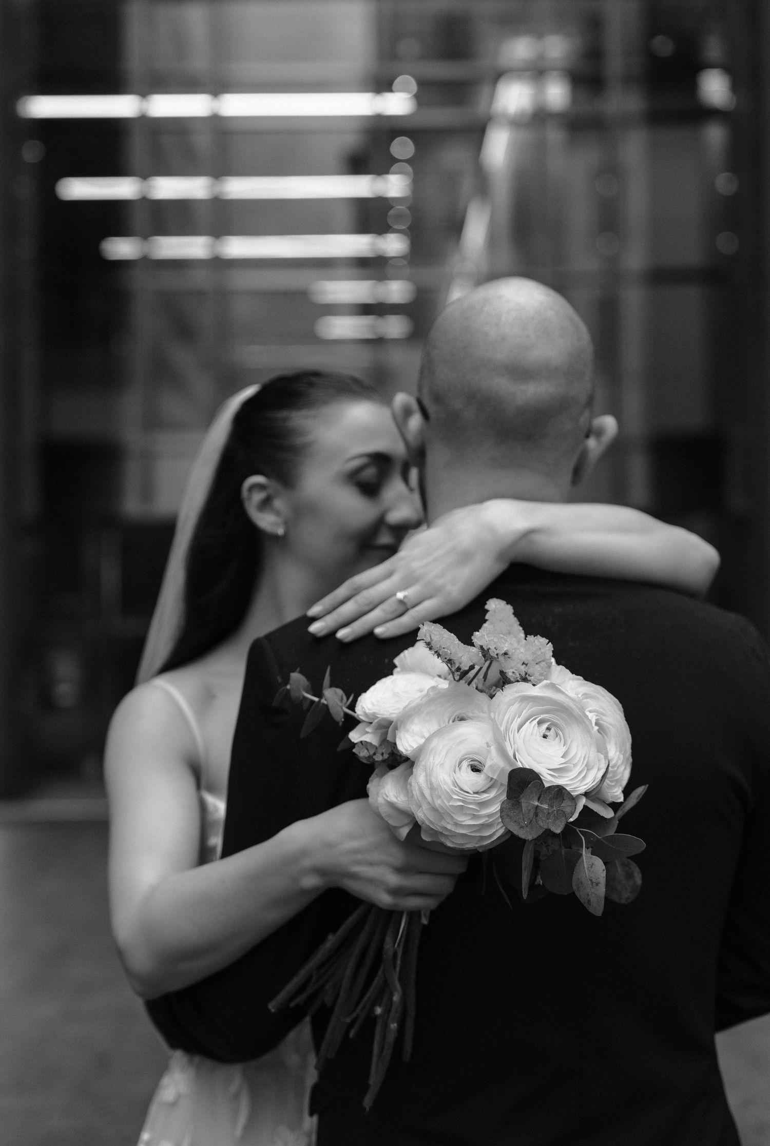 A romantic black and white wedding photo showing a couple embracing with a bouquet of white roses between them.