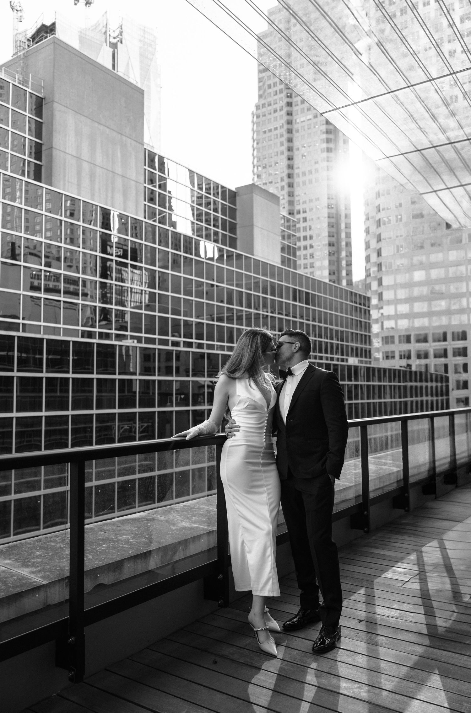 A couple poses for artistic black and white wedding photos in a modern architectural setting with glass windows.