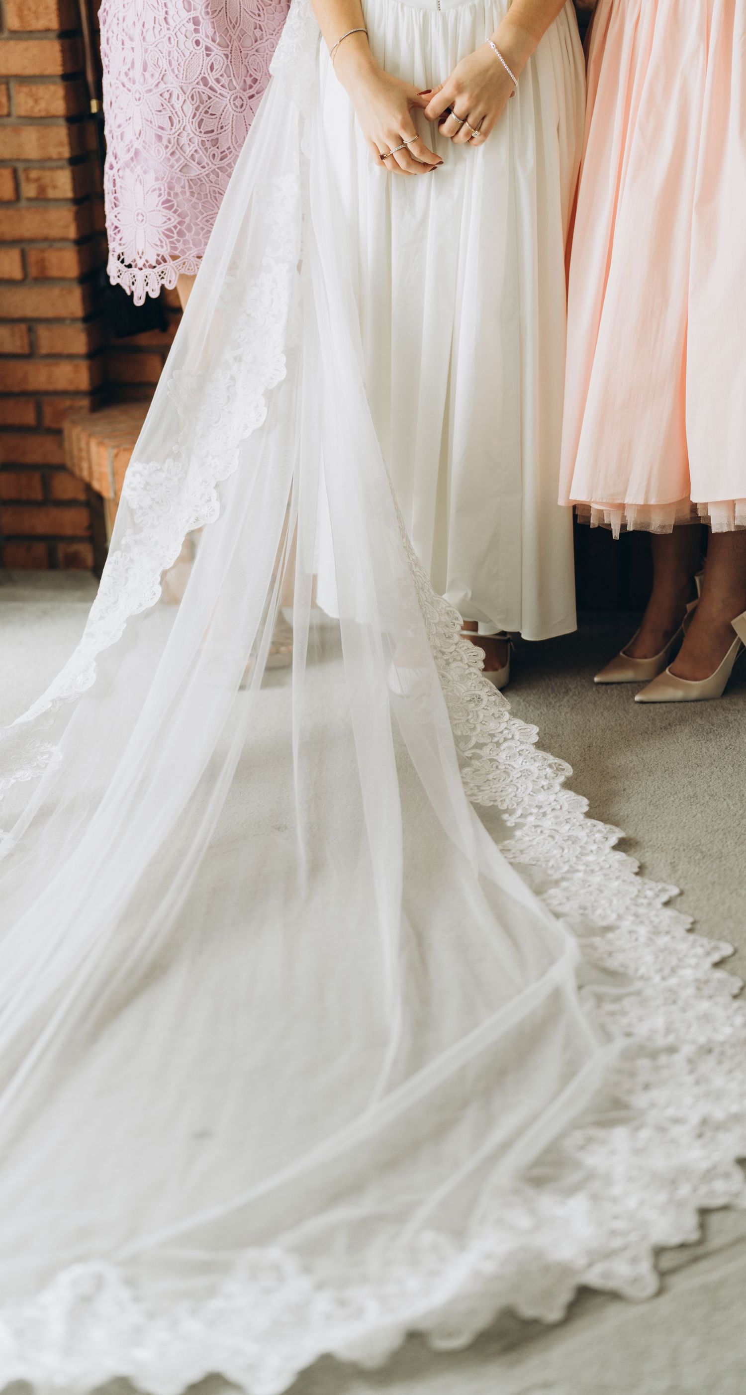 Elegant white wedding dress train with delicate lace detailing flows across grey floor.