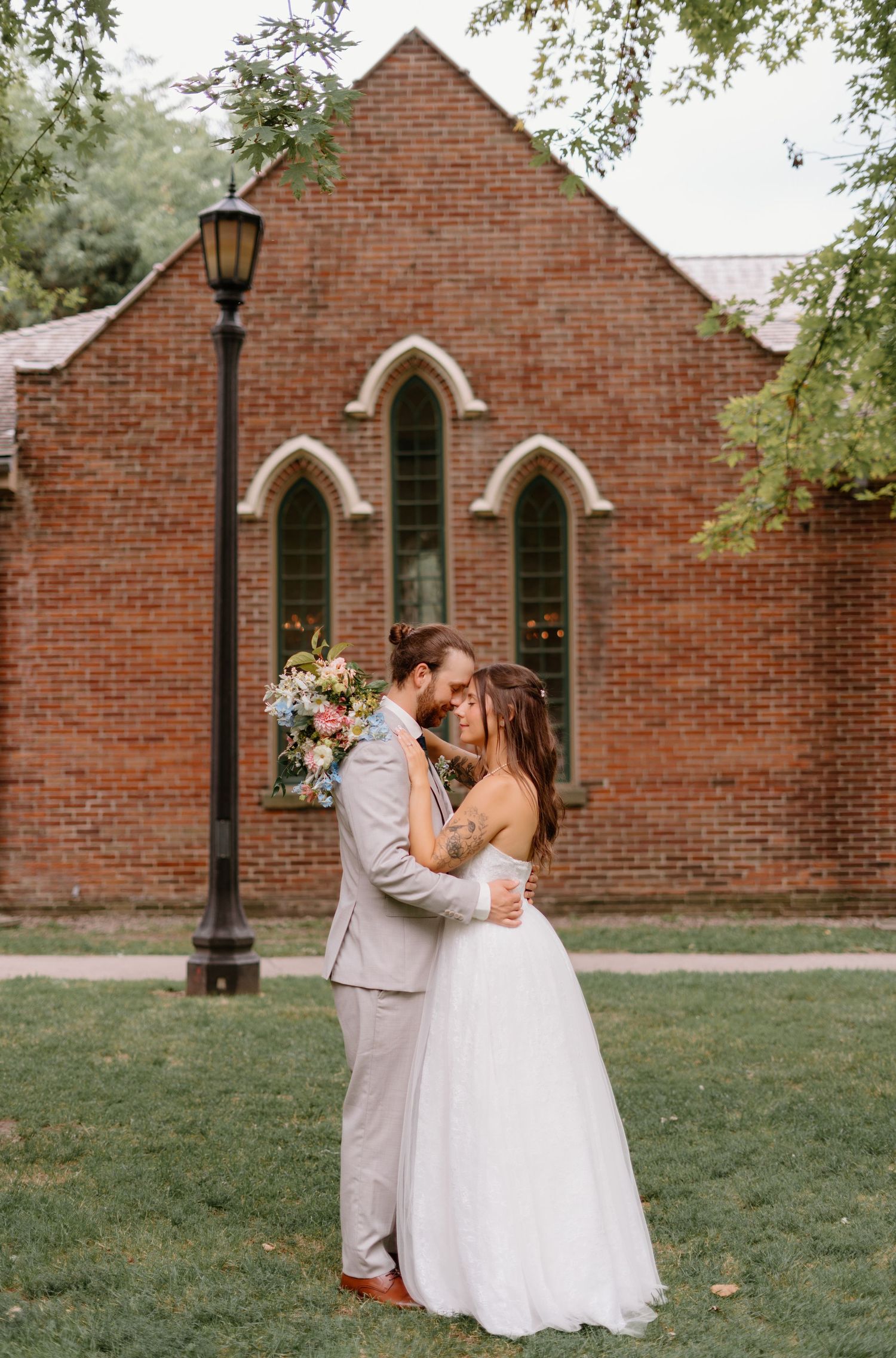 Romantic outdoor wedding portraits against a rustic brick church building with arched doorway and lamp post.