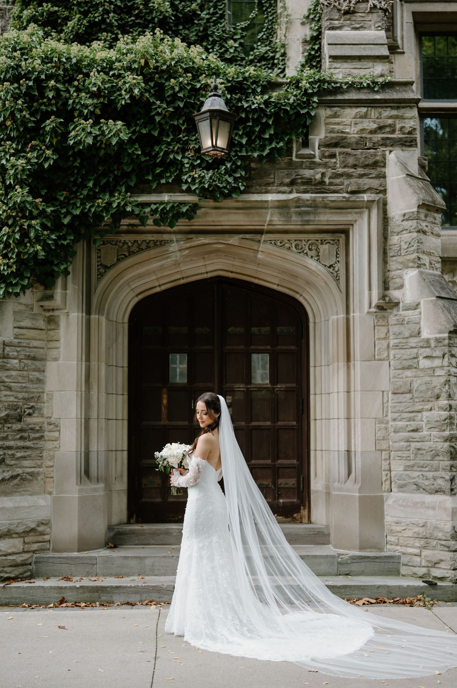 A bride in a flowing white gown and cathedral veil poses elegantly against a stone church entrance.