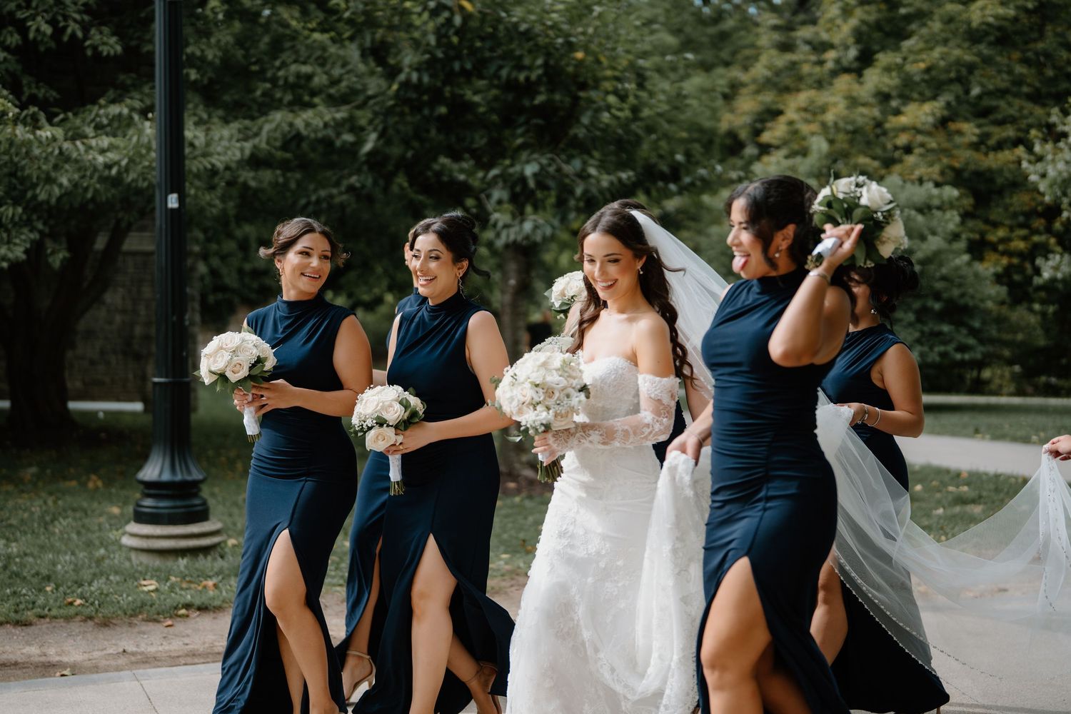 Wedding party in navy blue dresses and suits laughing together outdoors in a garden setting.