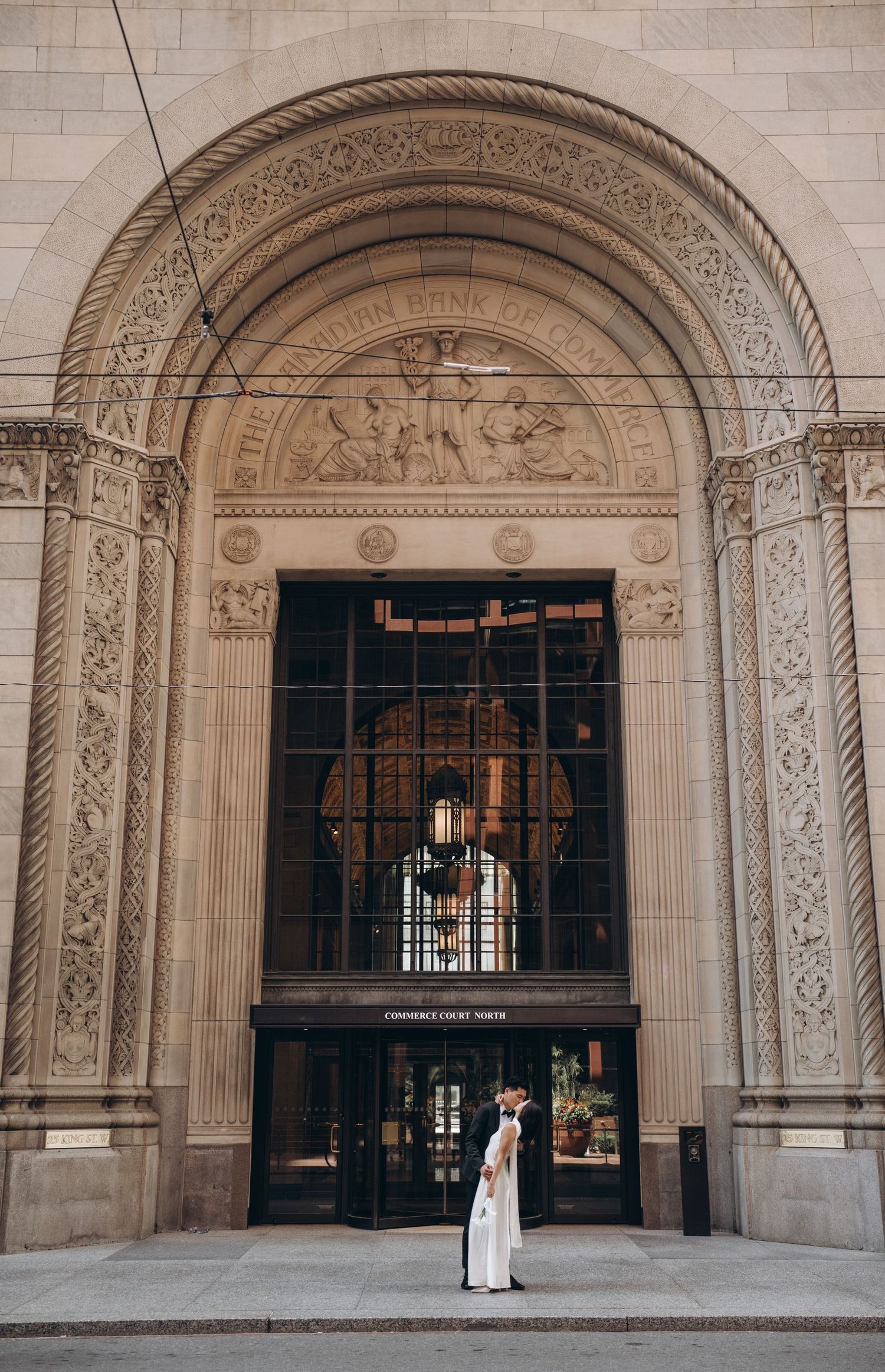 A person in white stands before an ornate archway entrance of a historic stone building with detailed architectural elements.