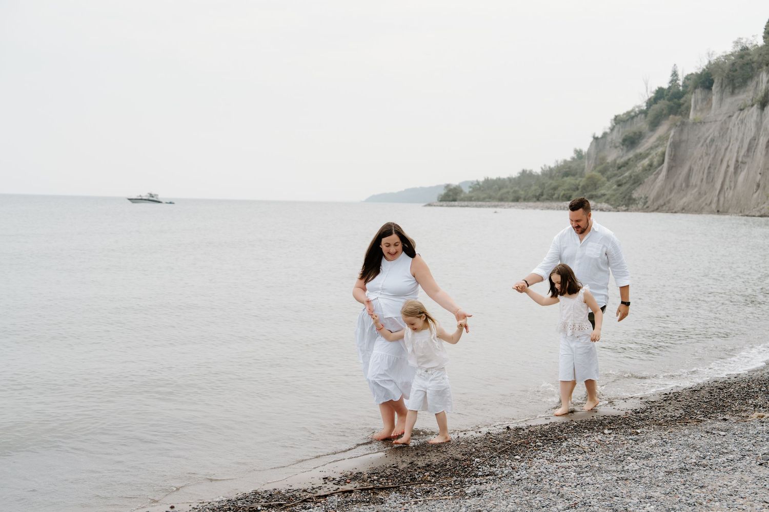 People in white outfits enjoying a playful moment on a rocky beach with cliffs and ocean in the background.