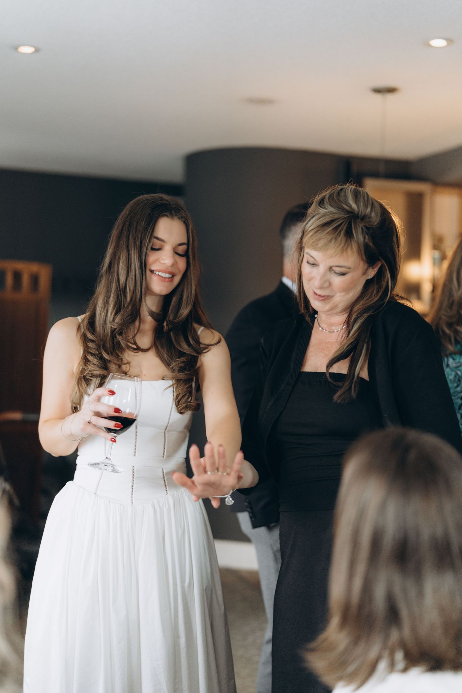 A woman in a white wedding dress smiles while holding a wine glass during a celebration.