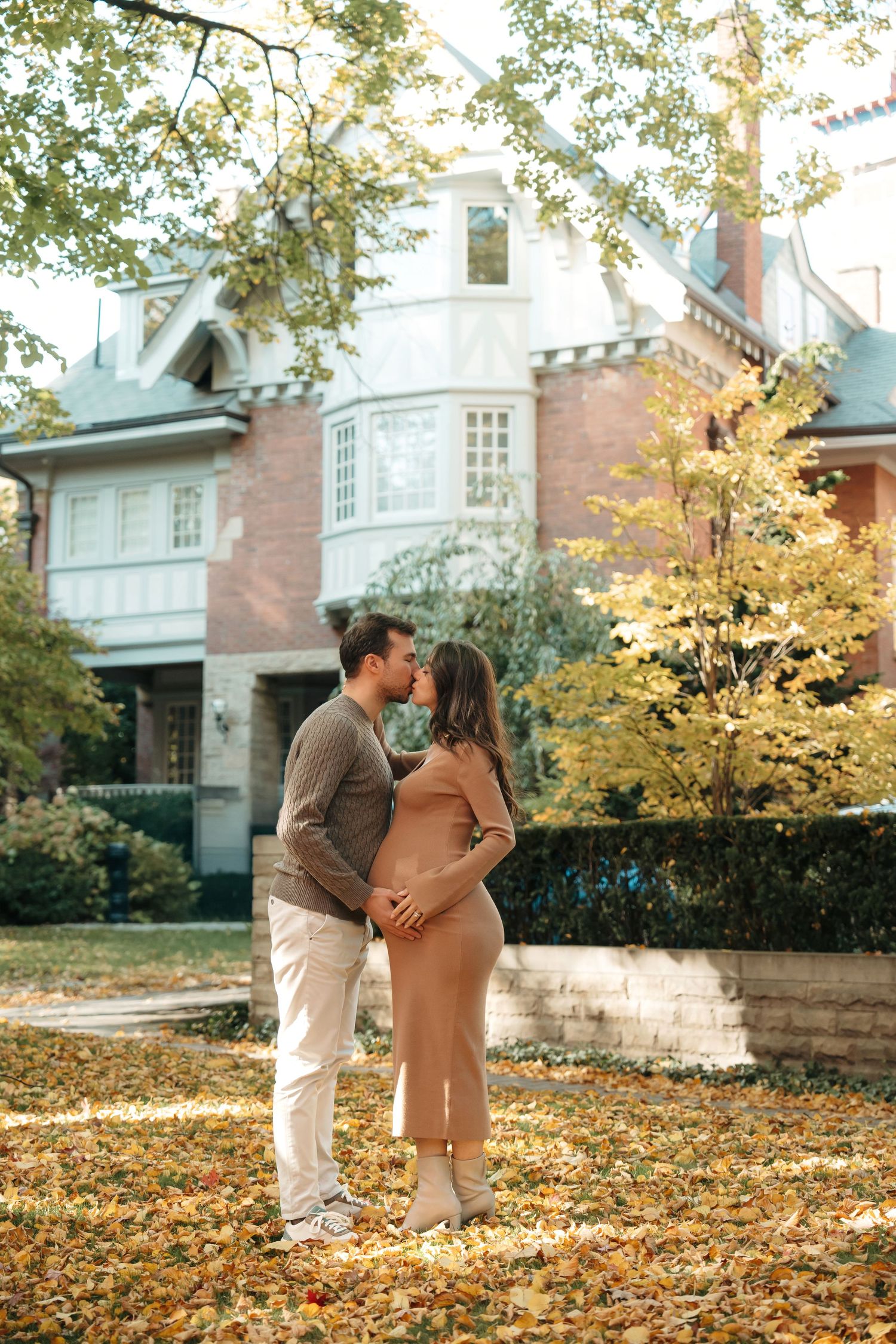 A romantic autumn scene outside a stately brick mansion with yellow leaves scattered on the ground.