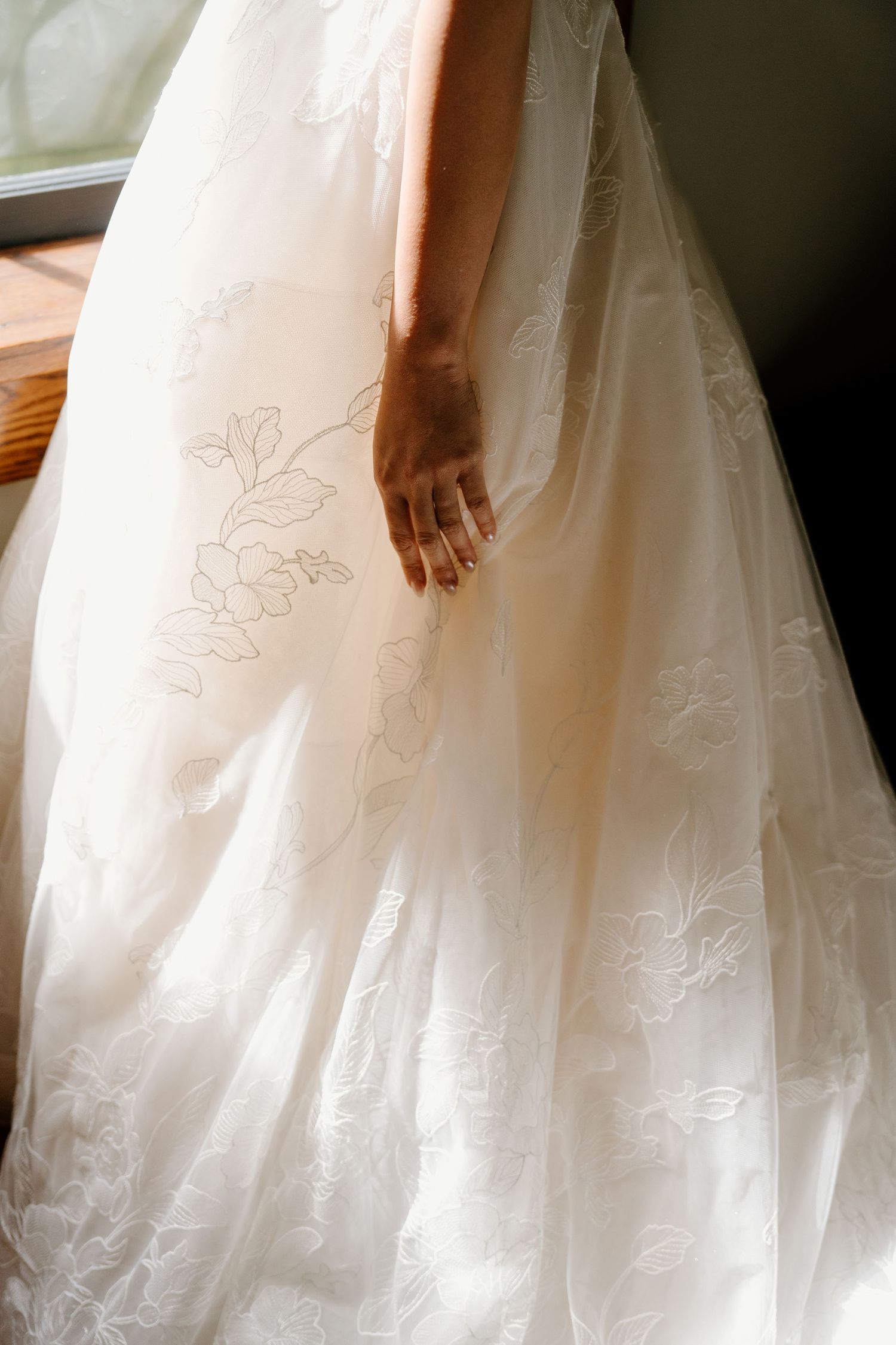 Close-up details of a white wedding dress with delicate embroidery and flowing tulle fabric in soft natural light.
