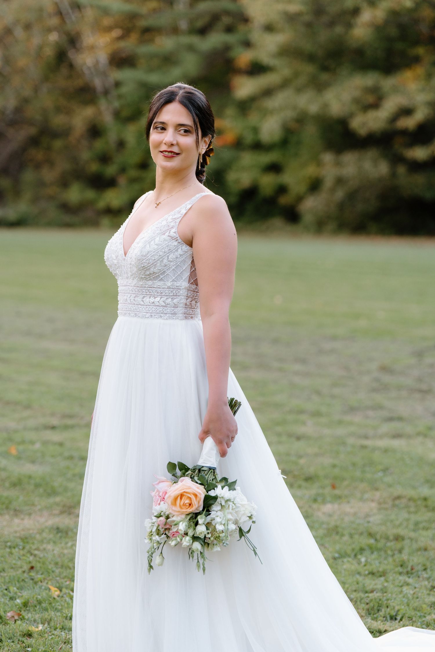 Full-length portrait of bride in white gown holding floral bouquet on grassy lawn.