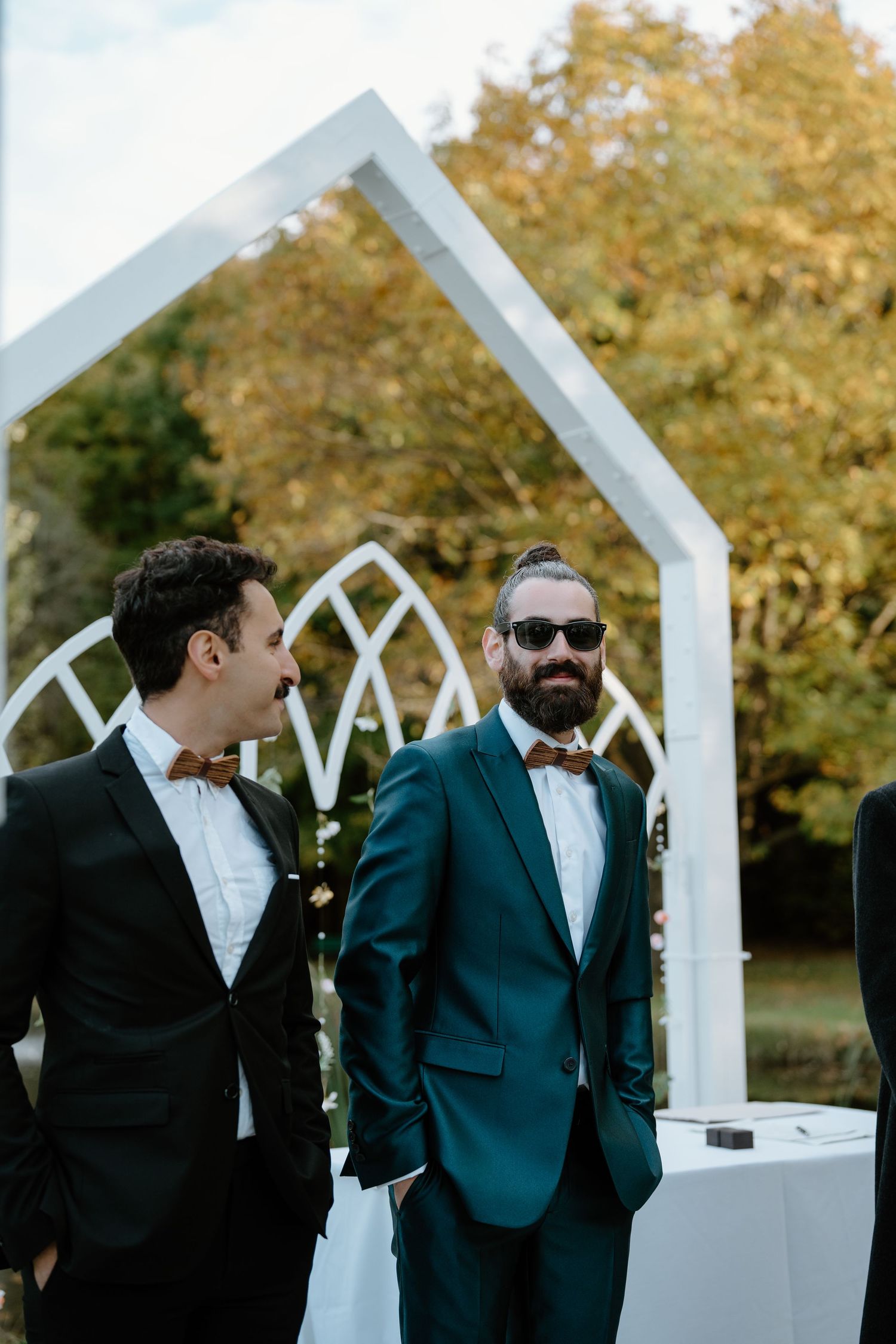 Wedding attendees in formal attire standing by modern white chapel structure.