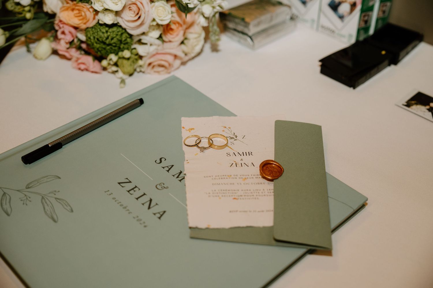 Wedding invitation suite with gold rings and sage green envelopes on white surface.