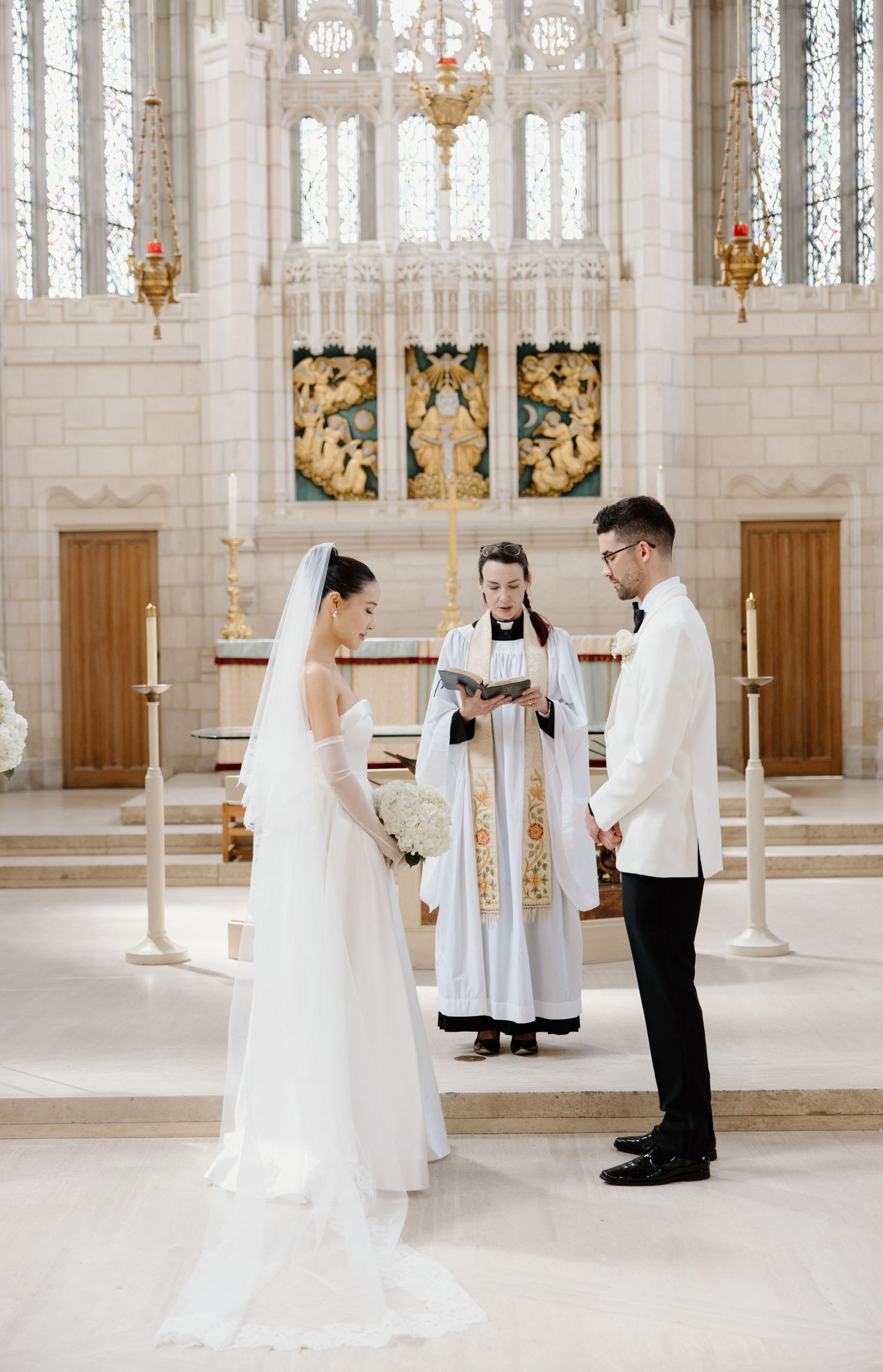 Traditional Catholic wedding ceremony taking place inside an ornate white church with elegant architectural details and soft lighting.