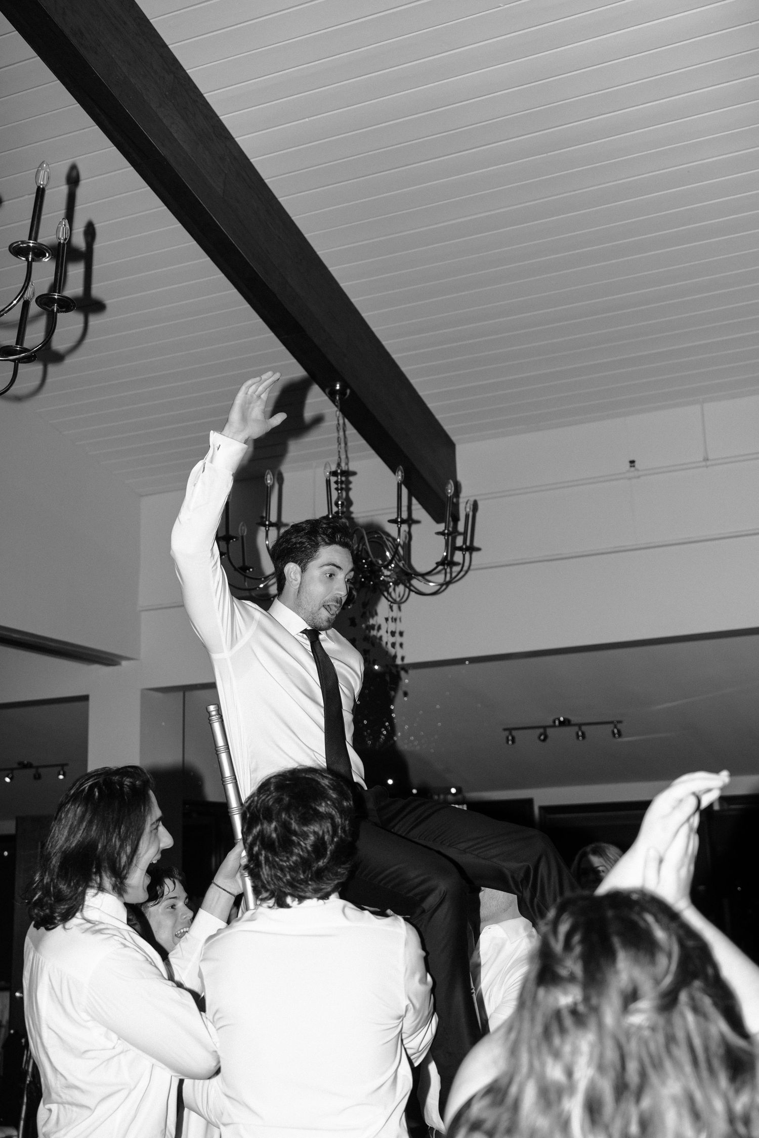 Wedding guests lift and celebrate on a dance floor during a reception party.