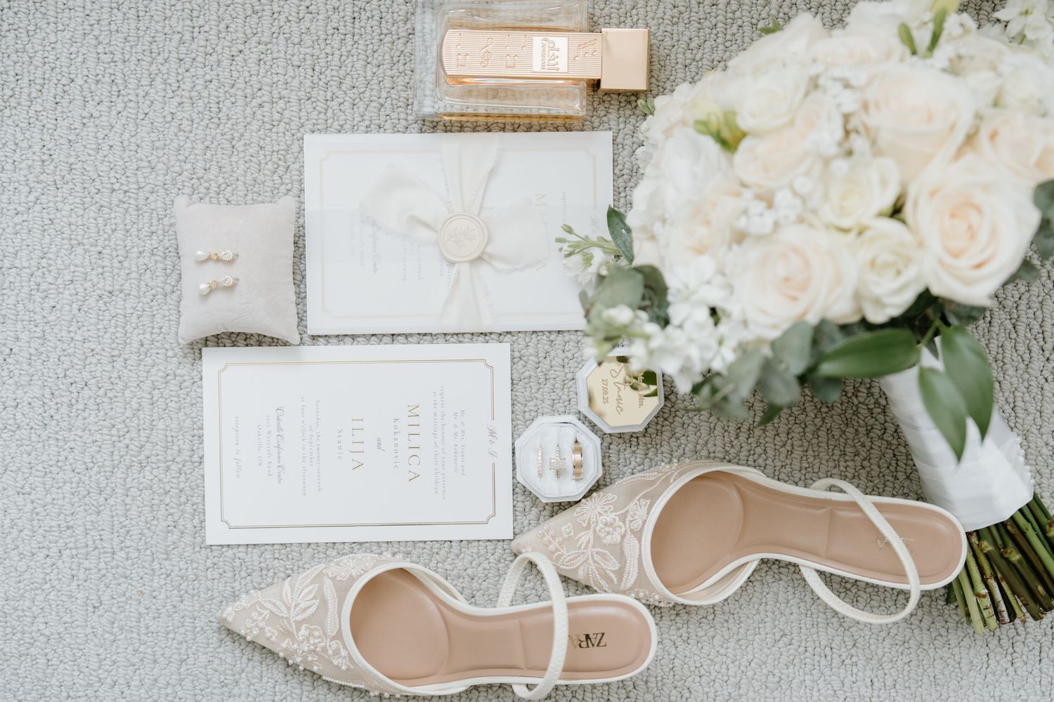 Elegant wedding invitation suite with white flowers, beige details, and delicate calligraphy on a light gray background.