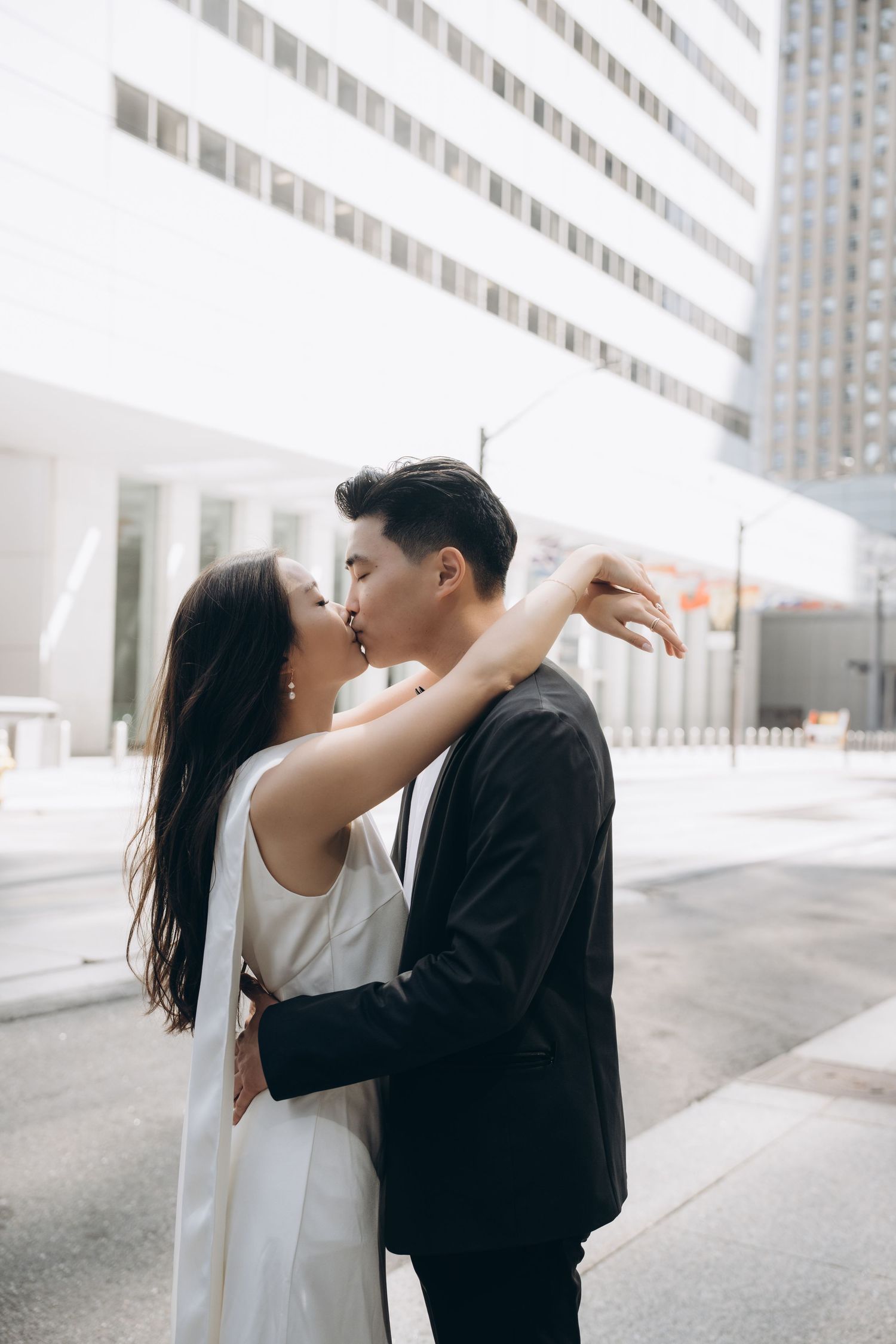 A tender embrace between a couple in formal attire against a modern urban backdrop.