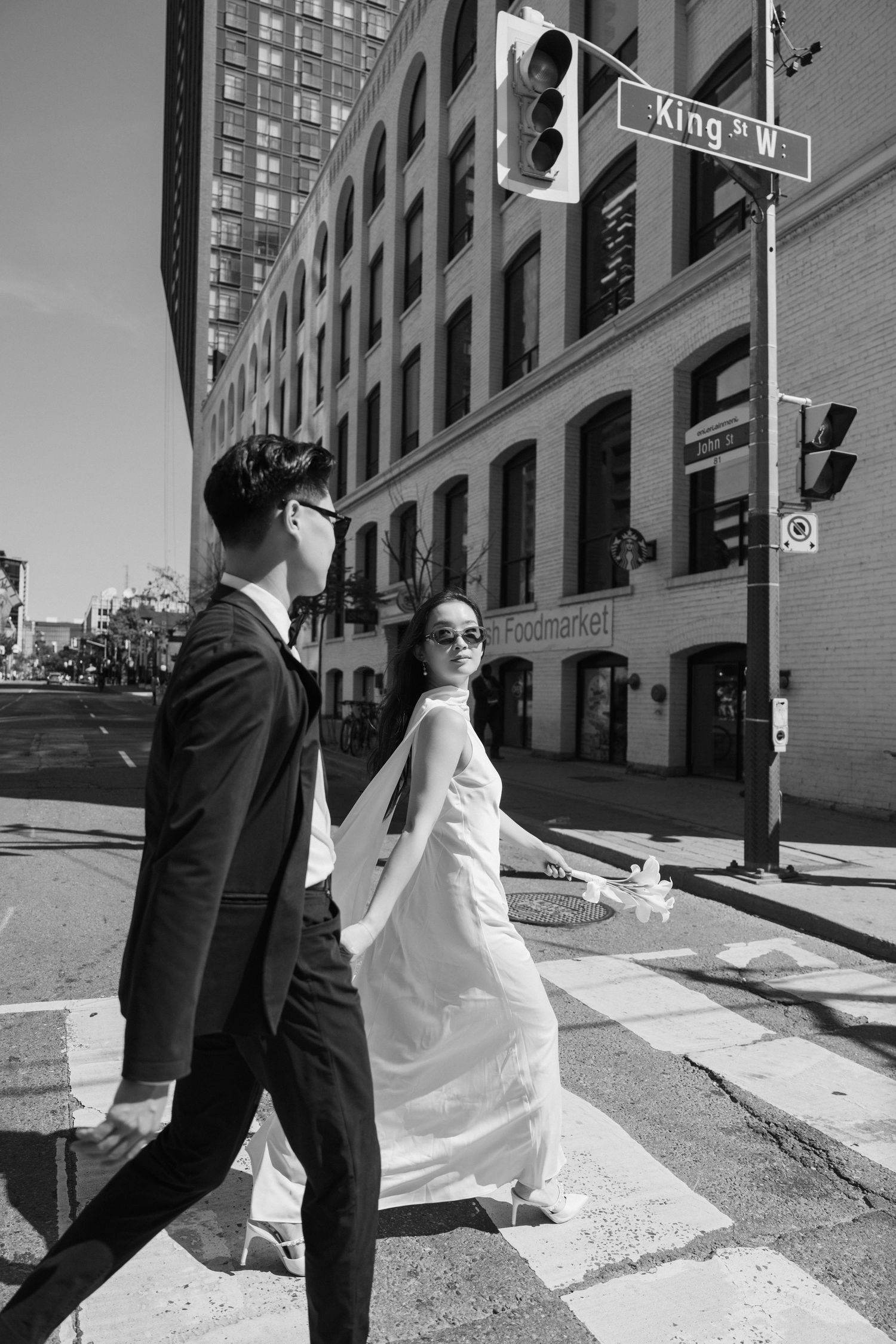 A stylish couple walks across an urban crosswalk near King Street with historic architecture in monochrome.