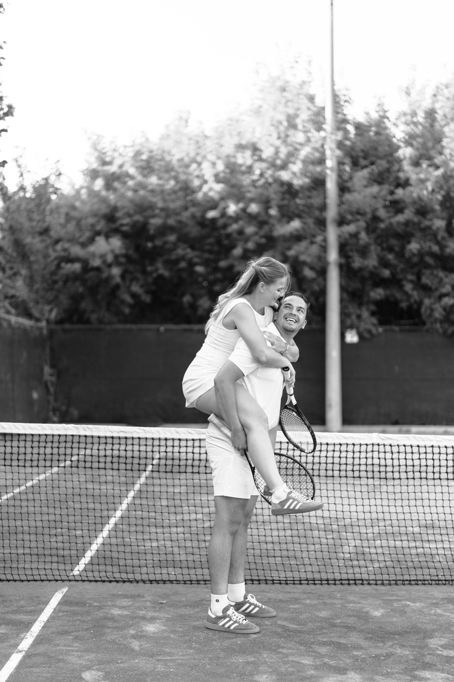 Two people lean over a tennis net for a tender moment during their match on the court.