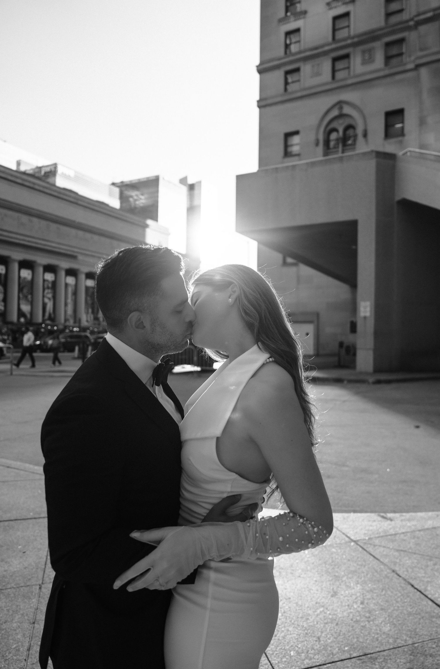 Four candid black and white photos capture a romantic wedding kiss sequence outside a city building.