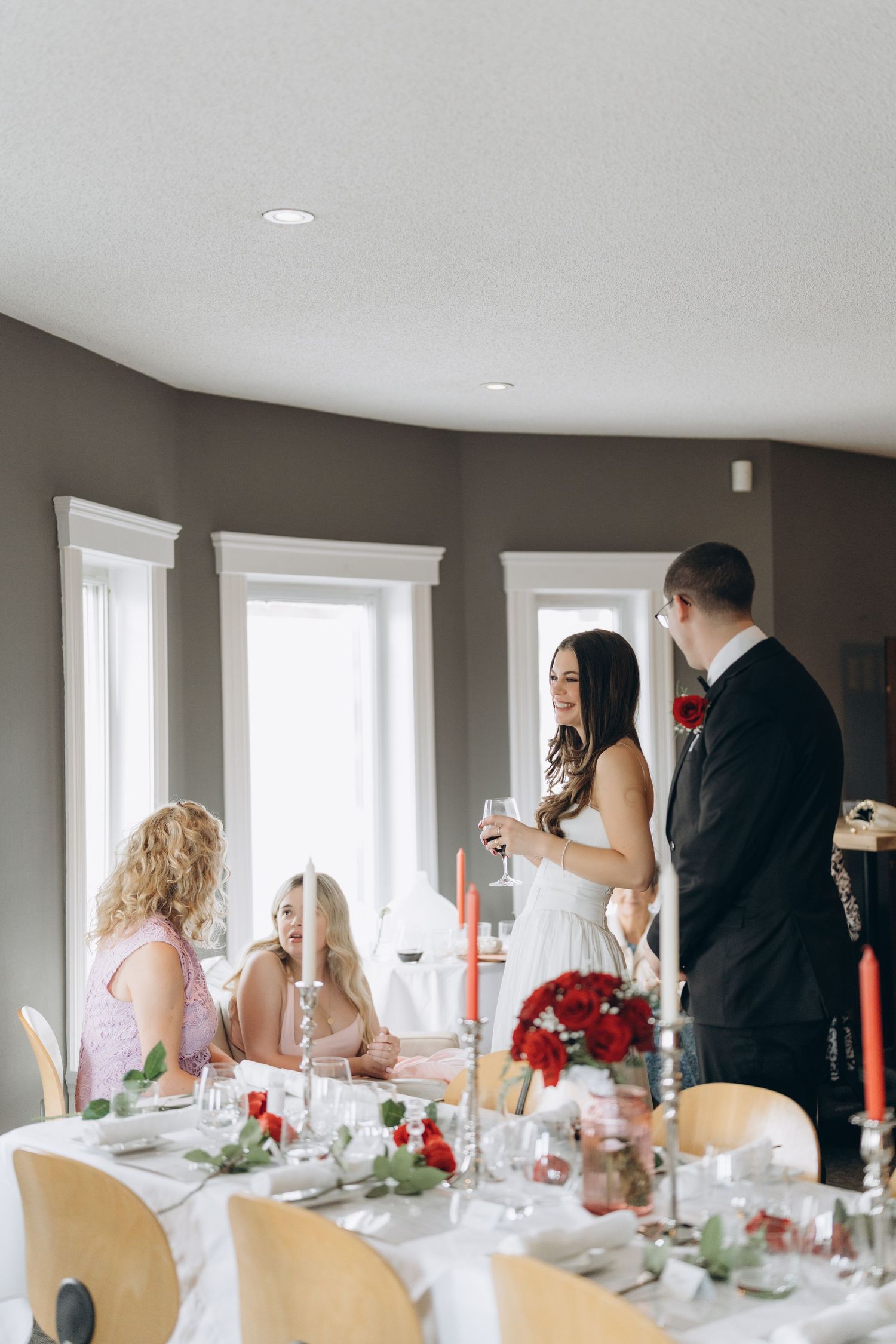 Wedding guests seated at an elegant reception table with white linens and red floral centerpieces.