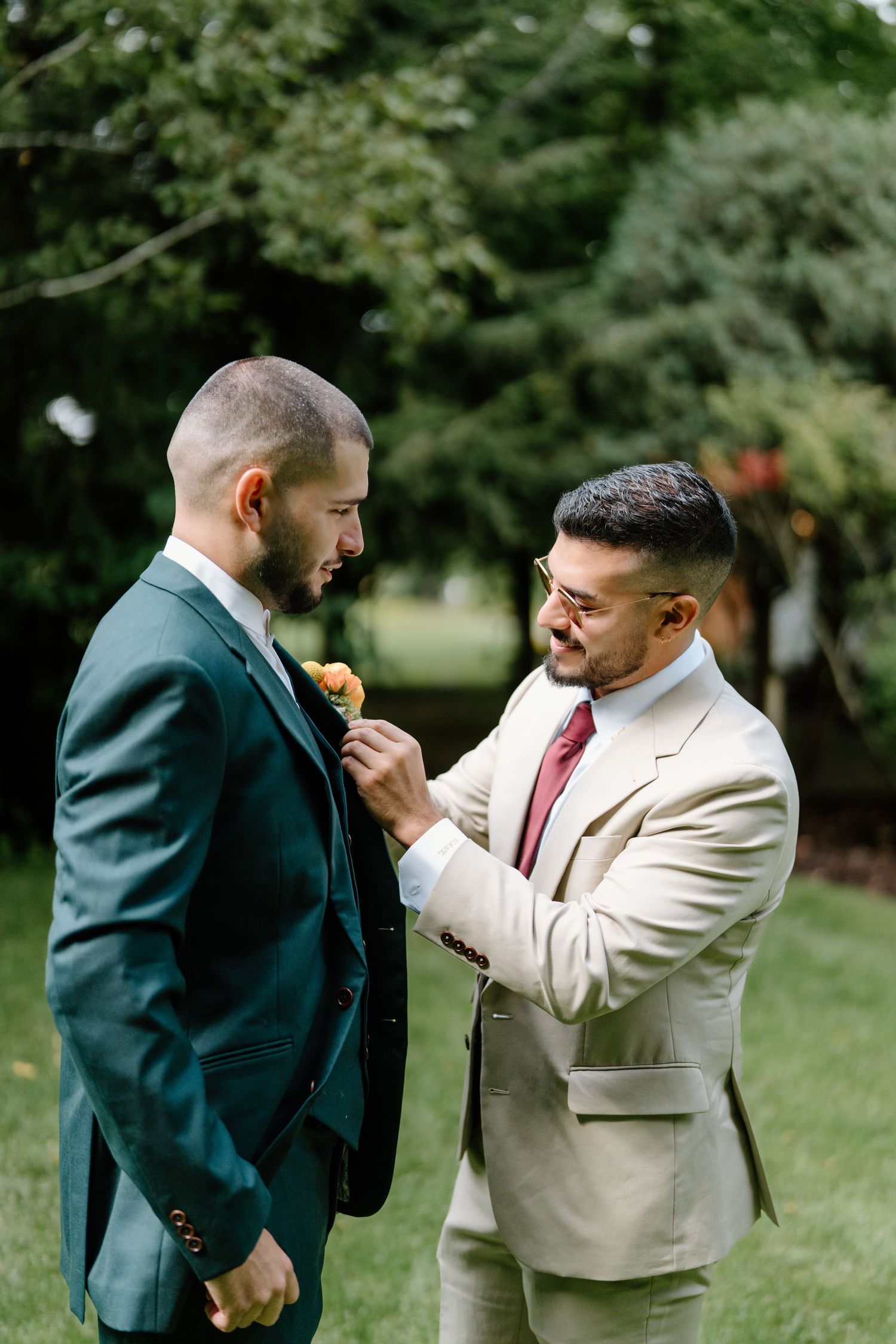 Two people in suits playfully square off in a mock boxing stance on a grassy outdoor area.