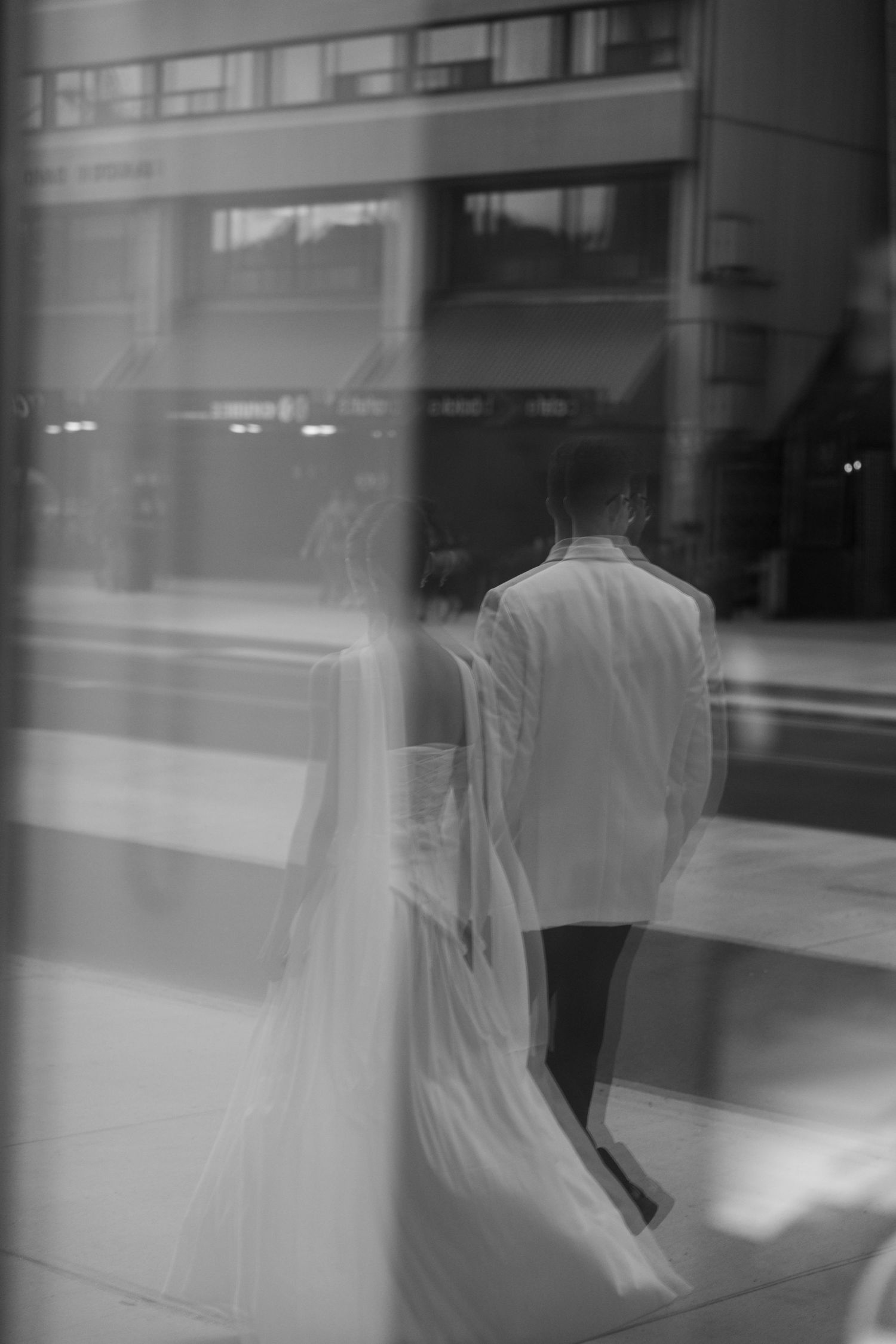 Artistic black and white photo of a person in white clothing viewed through glass with reflections.