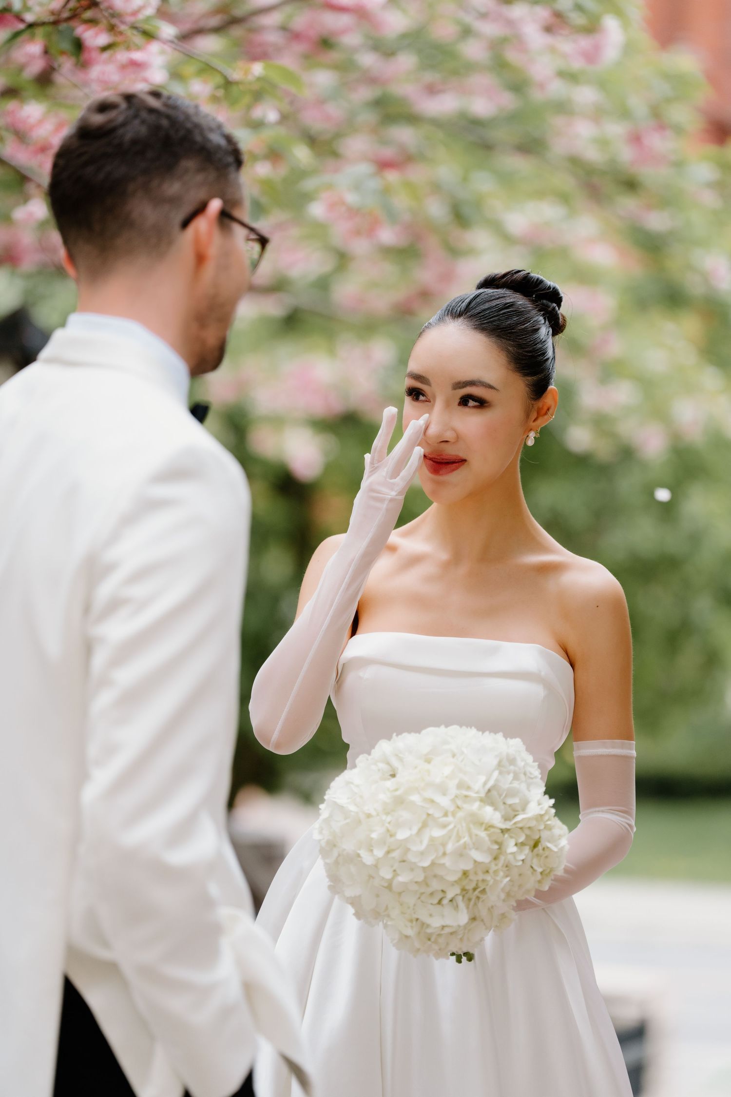 An emotional wedding first look moment in a garden with pink cherry blossoms and a beautiful white bouquet.