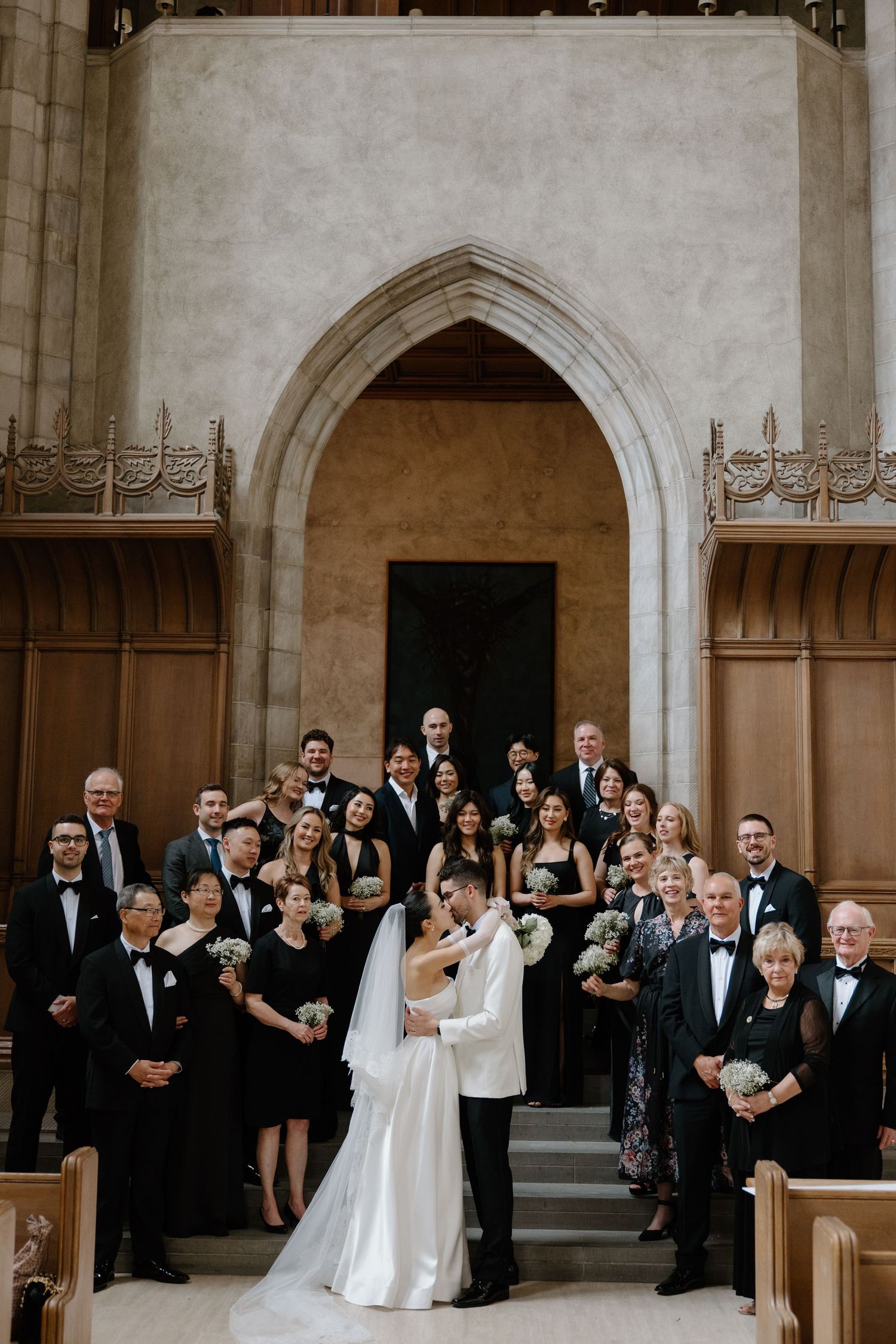 Wedding party gathers on church steps for formal group photo in elegant Gothic-style church entrance.