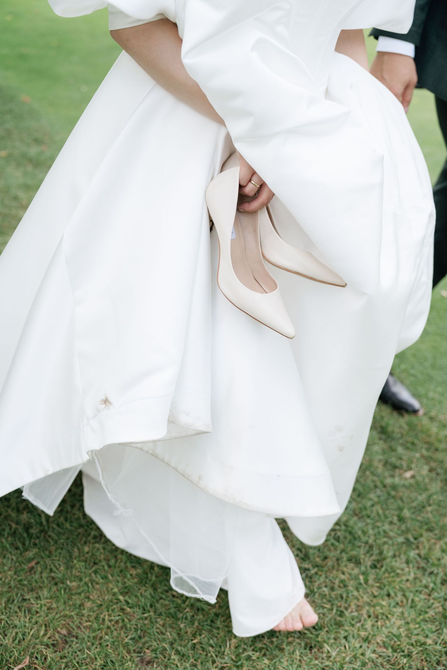 Candid shot of the bride holding her shoes while walking on the grass at Pheasant Run Golf Club, AZ Photo Studio.