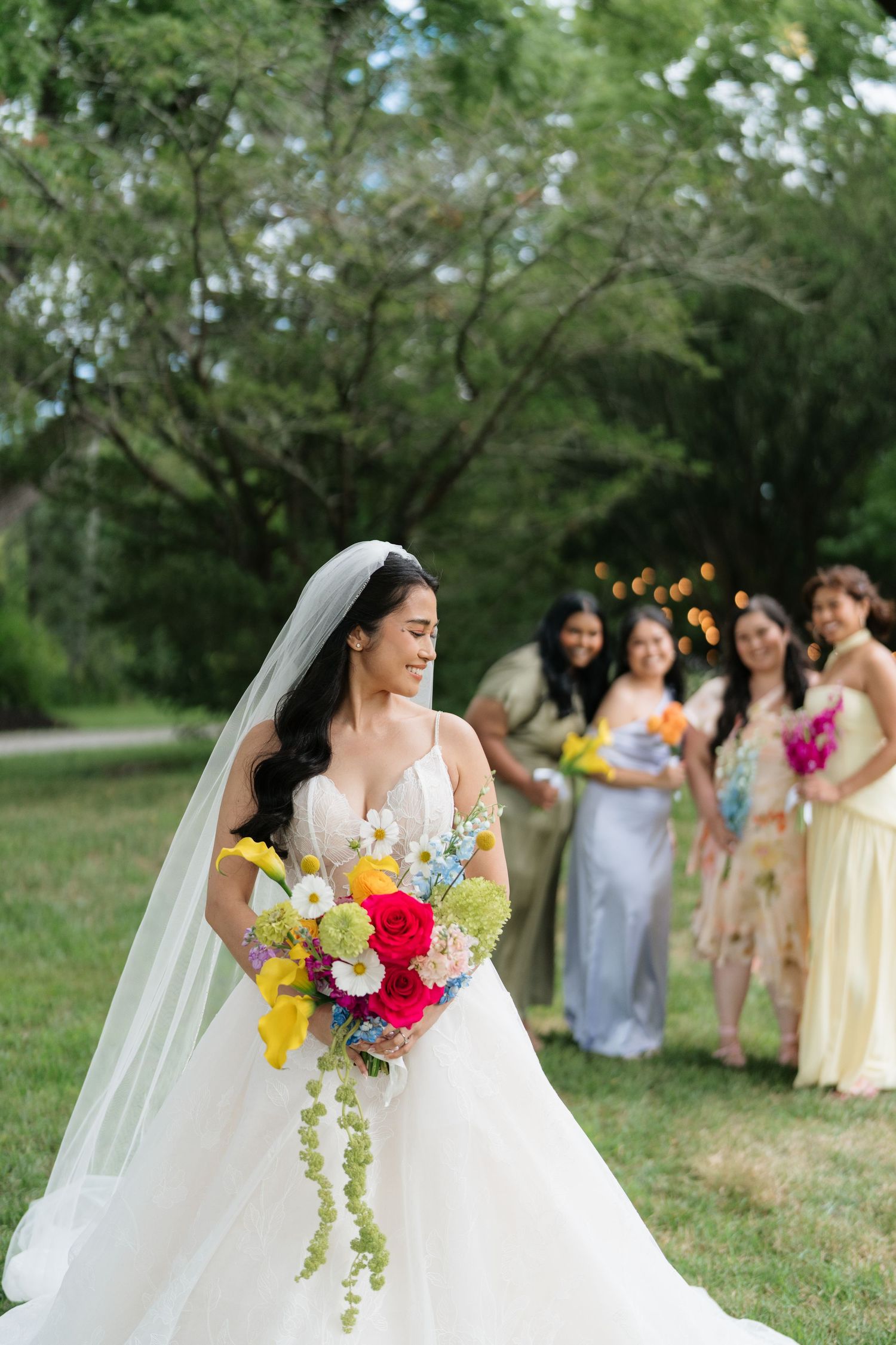 A bride in a flowing white gown holds a vibrant bouquet while bridesmaids in yellow dresses stand in the background.