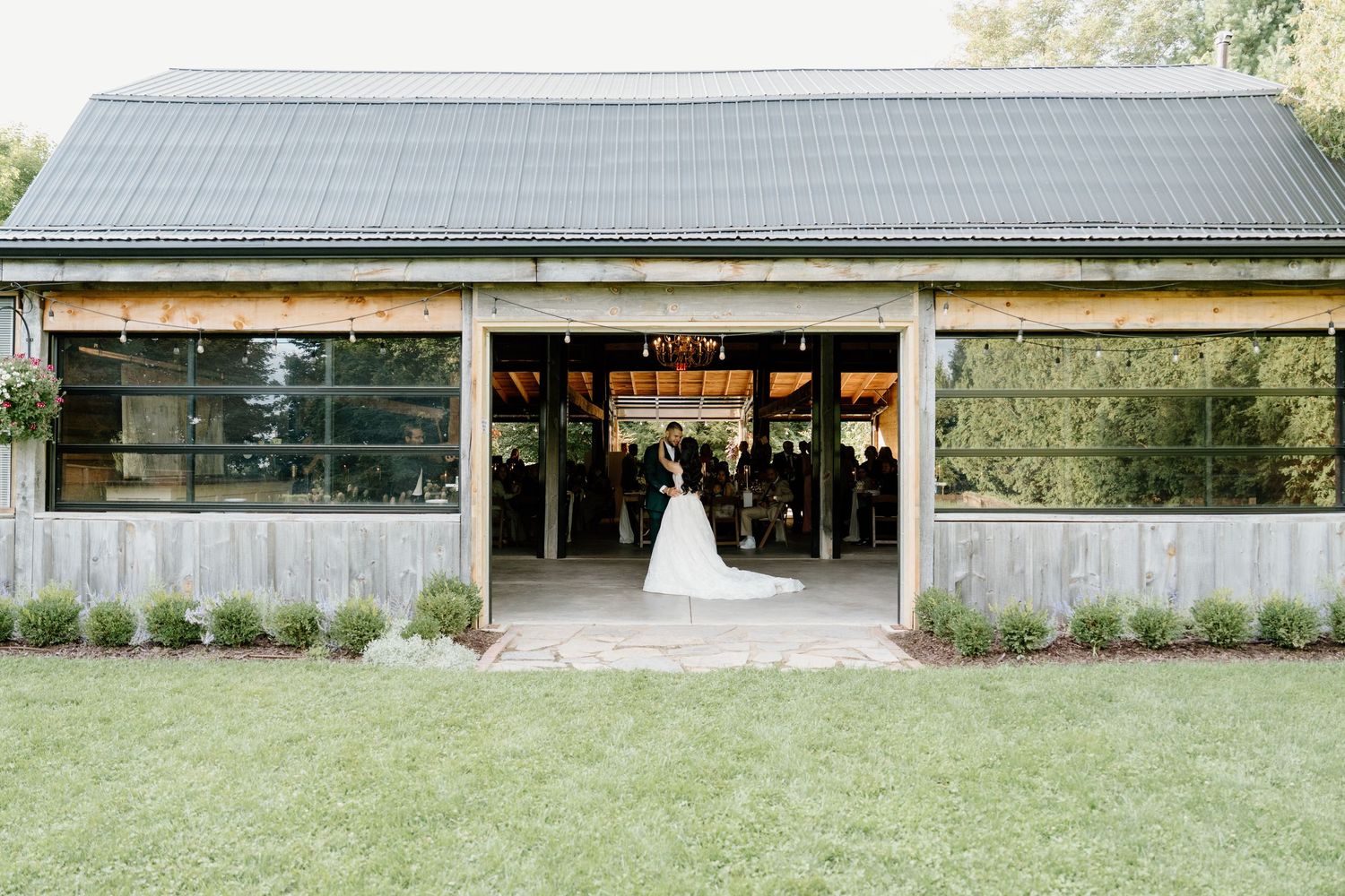 A panoramic view of a rustic barn venue with white trim and green landscaping on a sunny day.