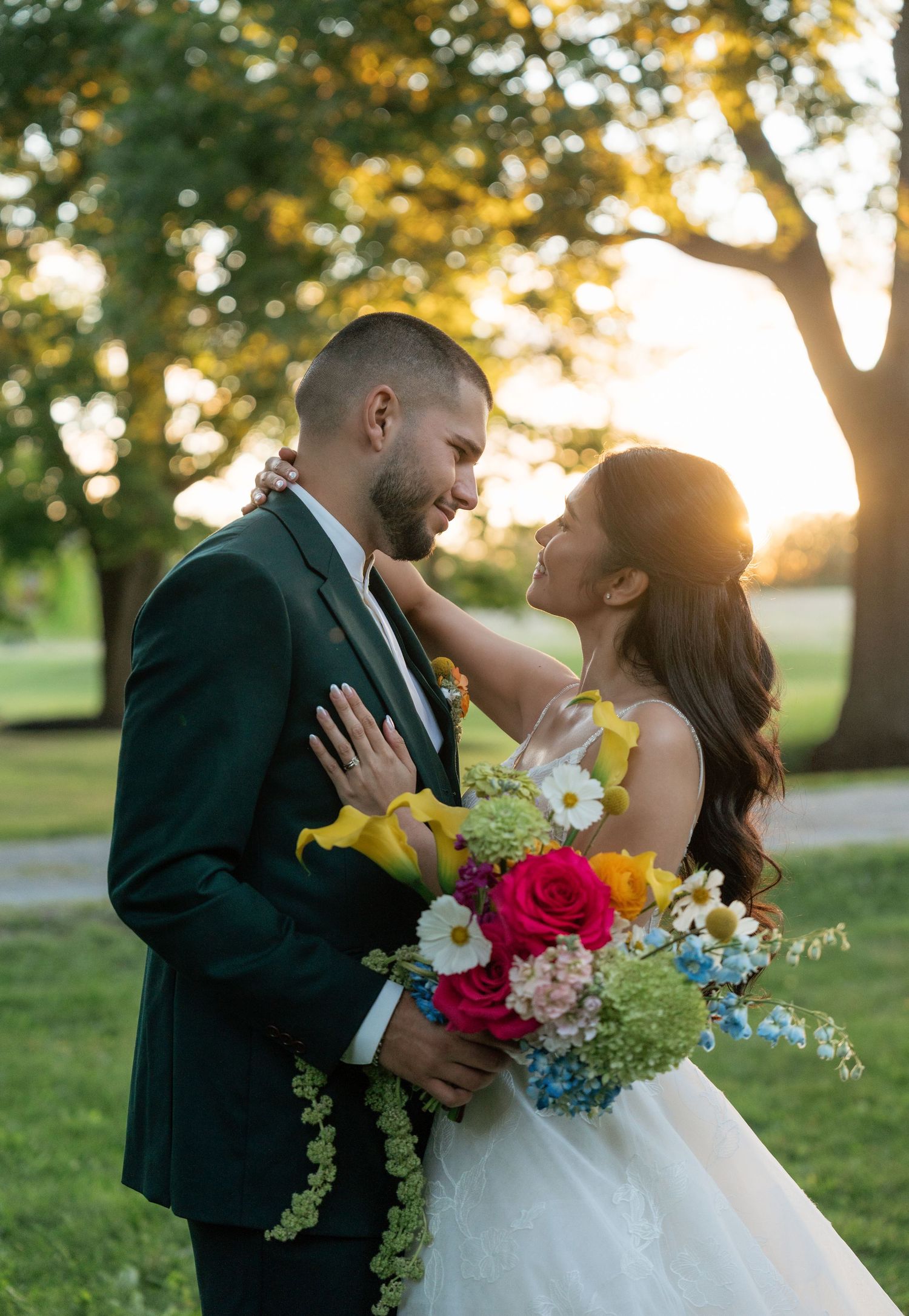 Romantic sunset wedding portrait with couple embracing in park surrounded by golden sunlight and colorful bouquet.