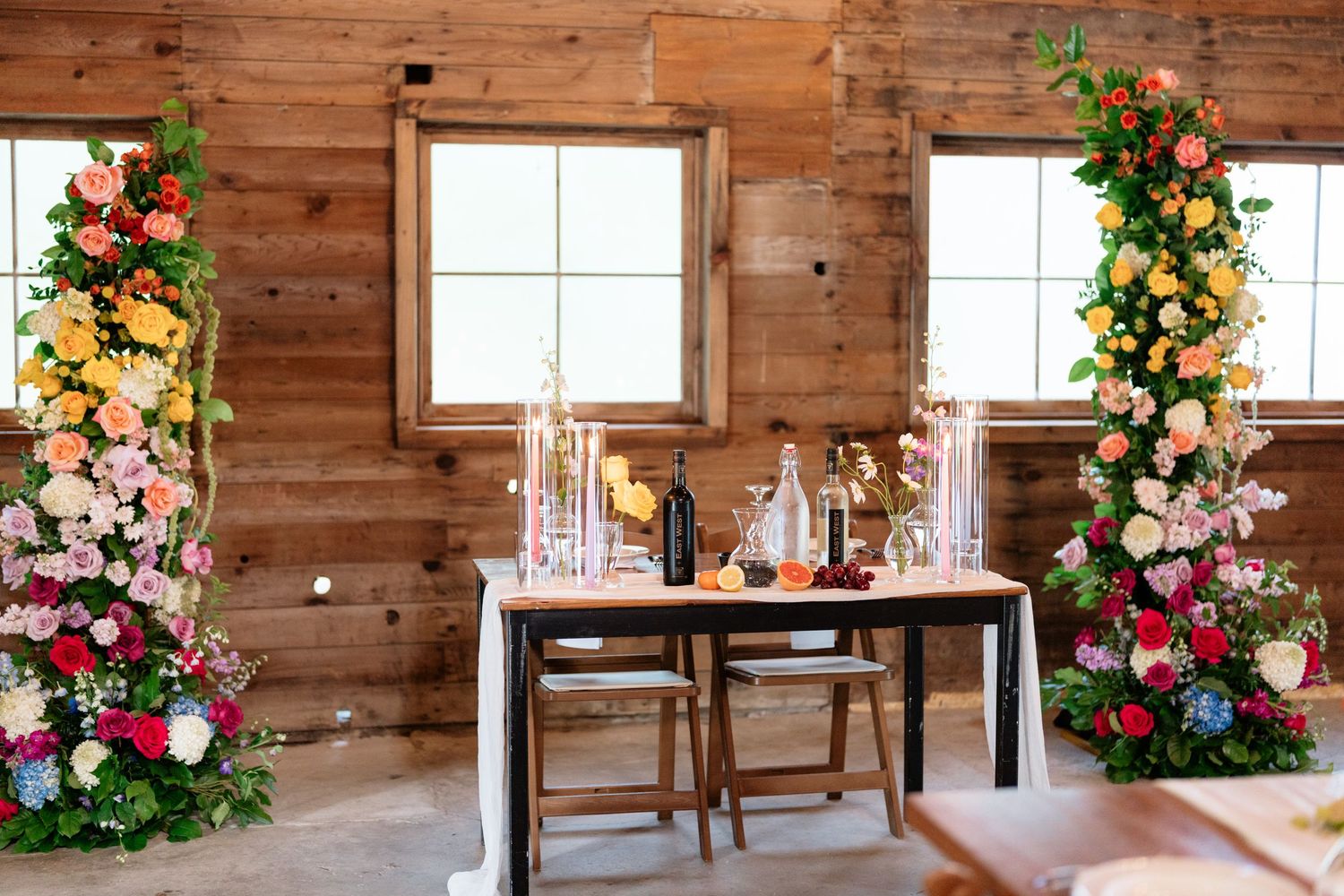 Rustic wooden interior of a barn or cabin decorated with colorful floral arrangements and white window frames.