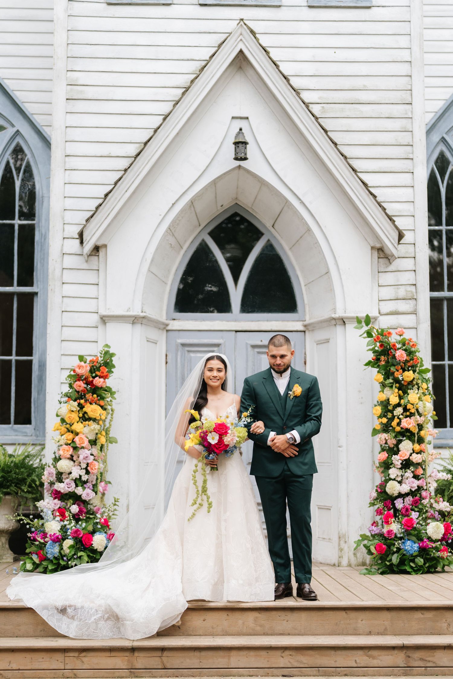 Elegant wedding photos at a white chapel with Gothic arched doorways decorated with vibrant floral arrangements.