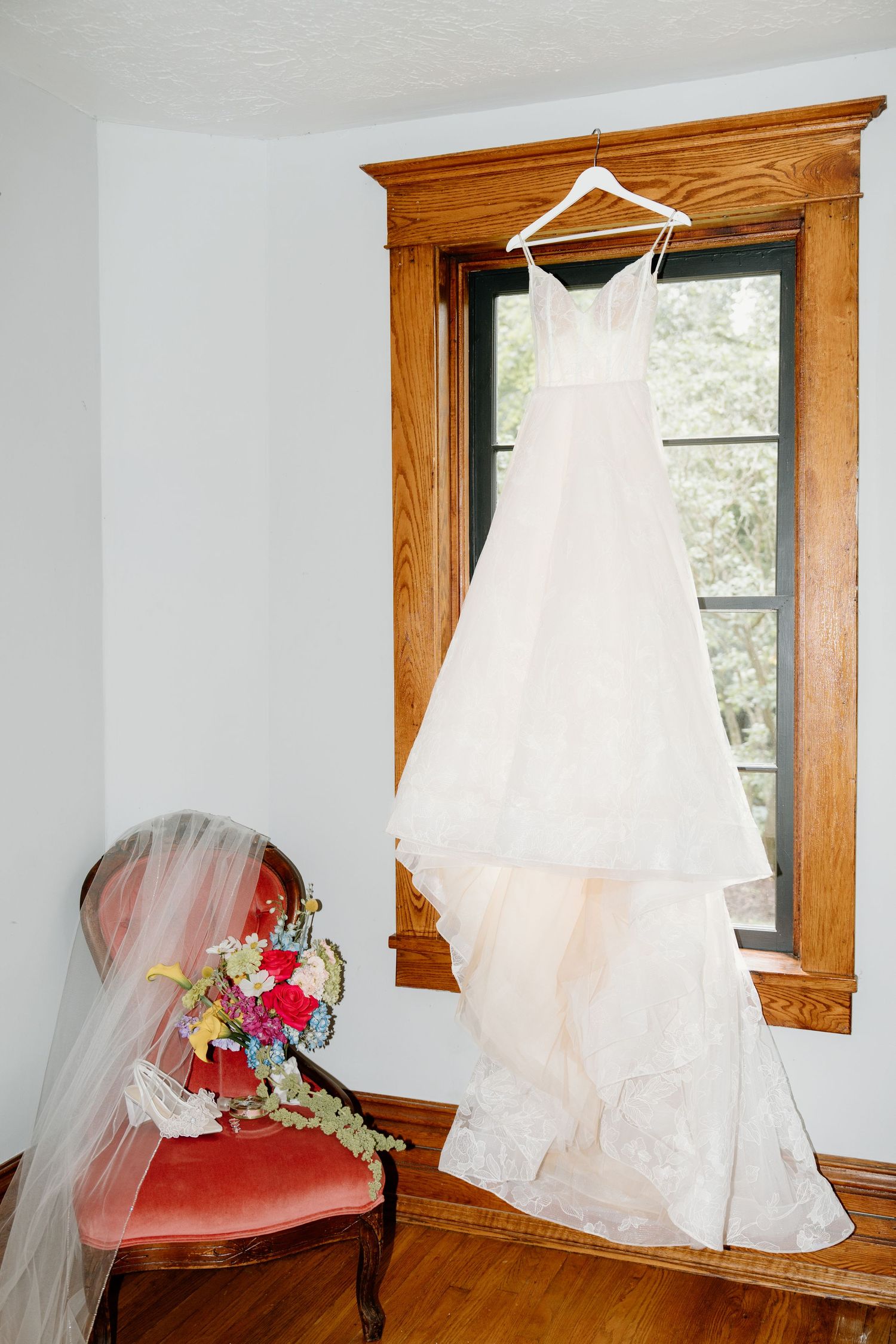 White wedding dress with flowing veil displayed against wooden window frames in natural lighting.