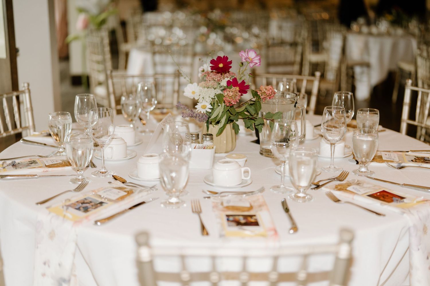 Elegant wedding reception table settings with white linens, glassware and pink floral centerpieces.
