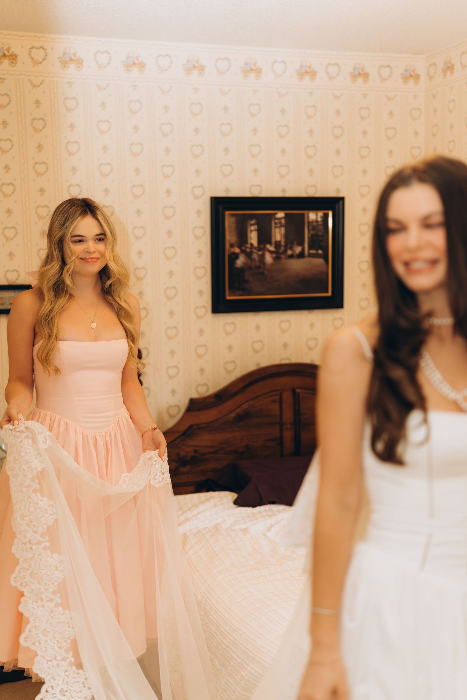 Bridesmaids in white and pink dresses gather in a room with patterned wallpaper.