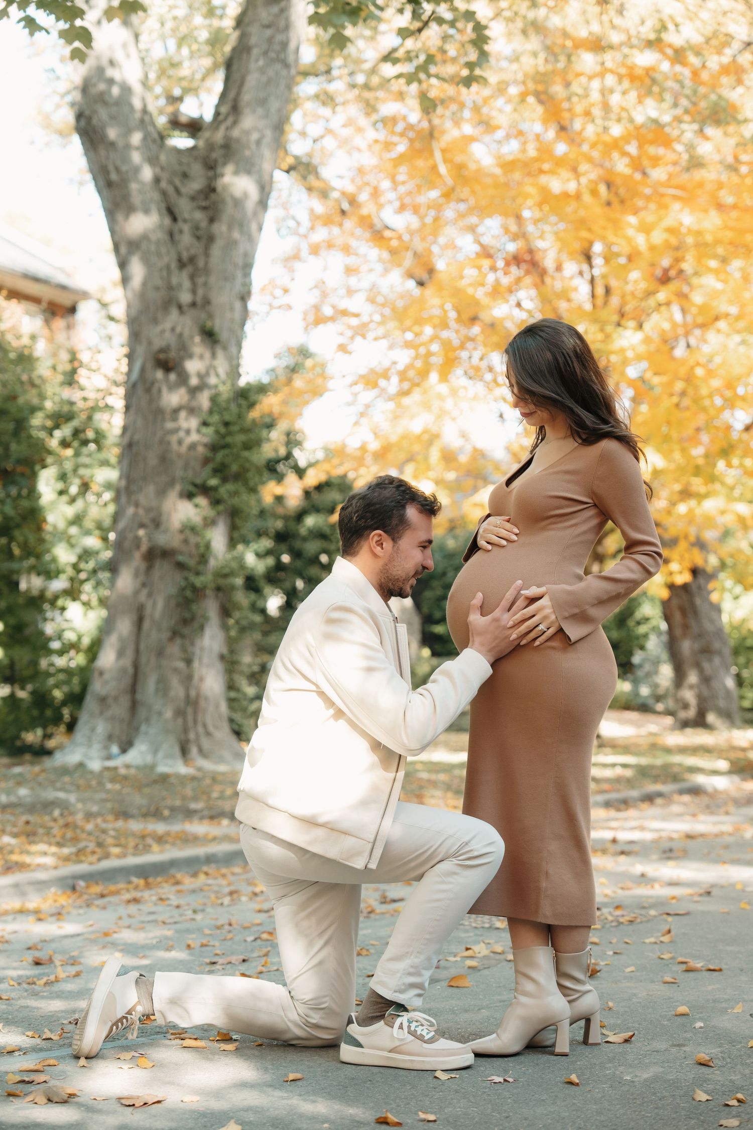 A heartwarming proposal moment captured in a fall setting with golden leaves and trees in the background.