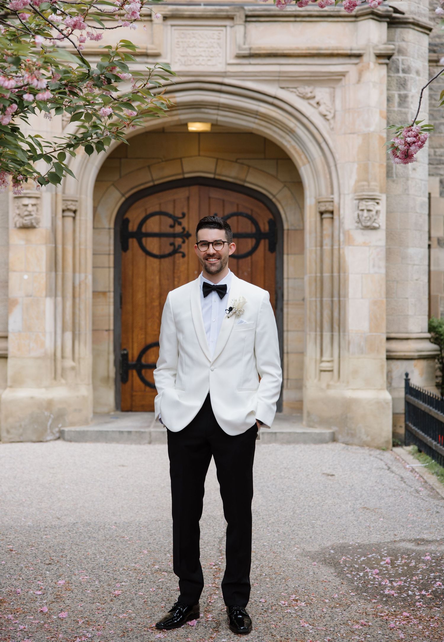 A figure in a classic white dinner jacket and black bow tie stands in front of an ornate arched stone doorway.