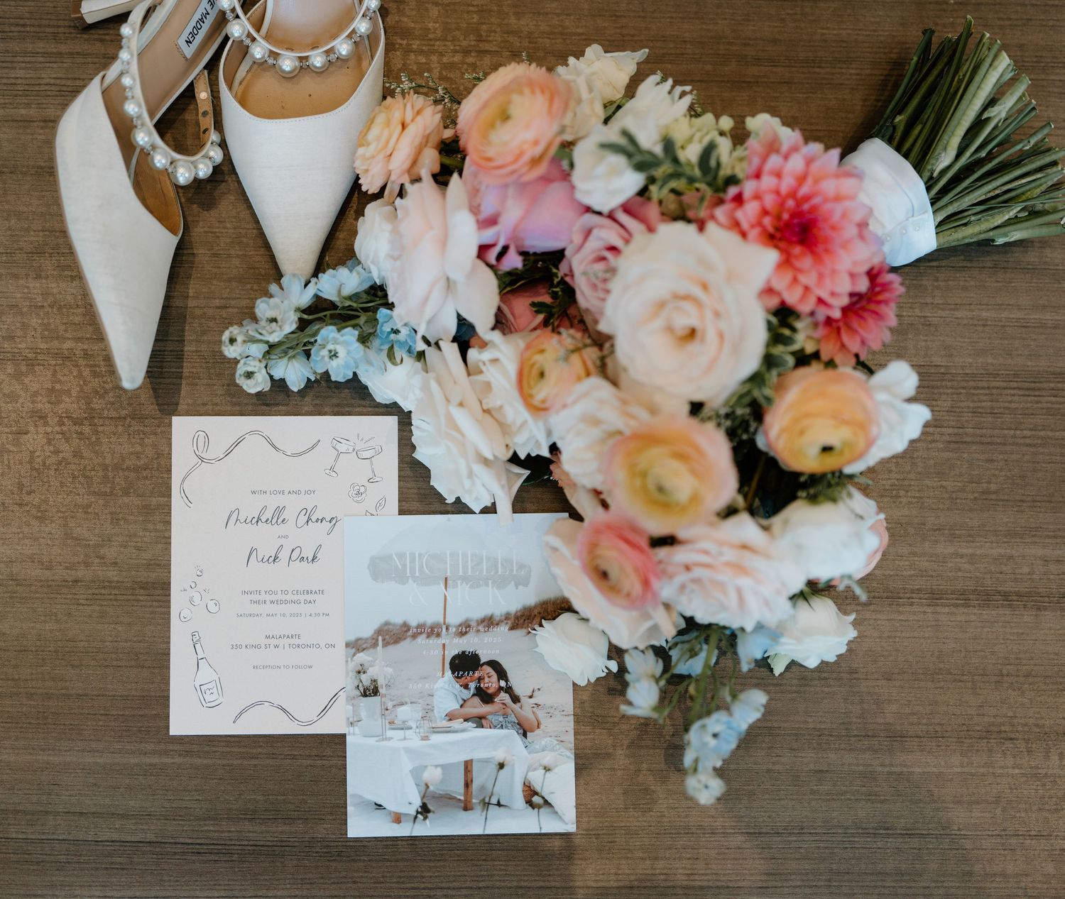 Elegant wedding stationery and delicate pink and peach floral arrangements displayed on rustic wooden surface.