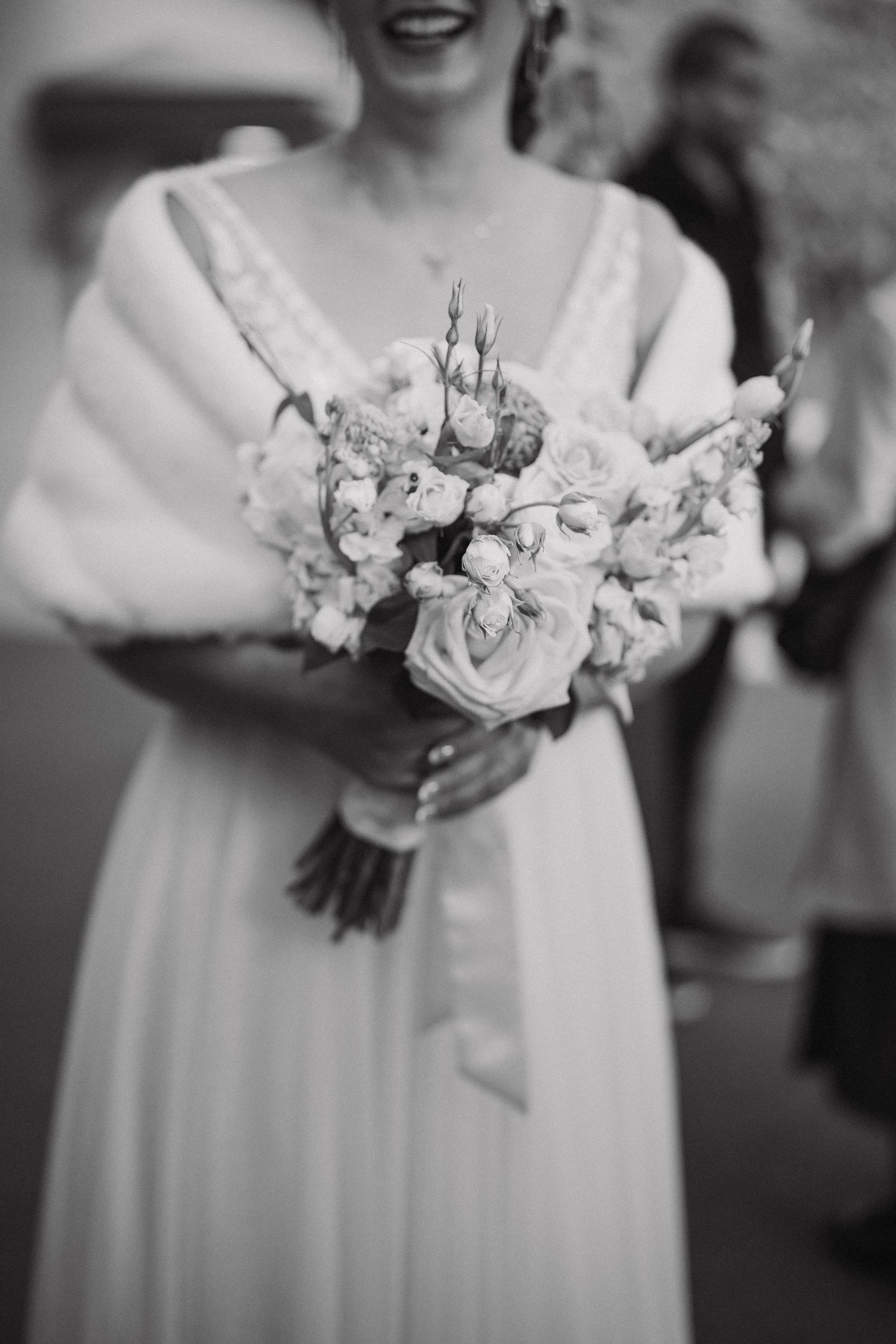 Close-up of wedding bouquet with white and pink flowers held against white dress.