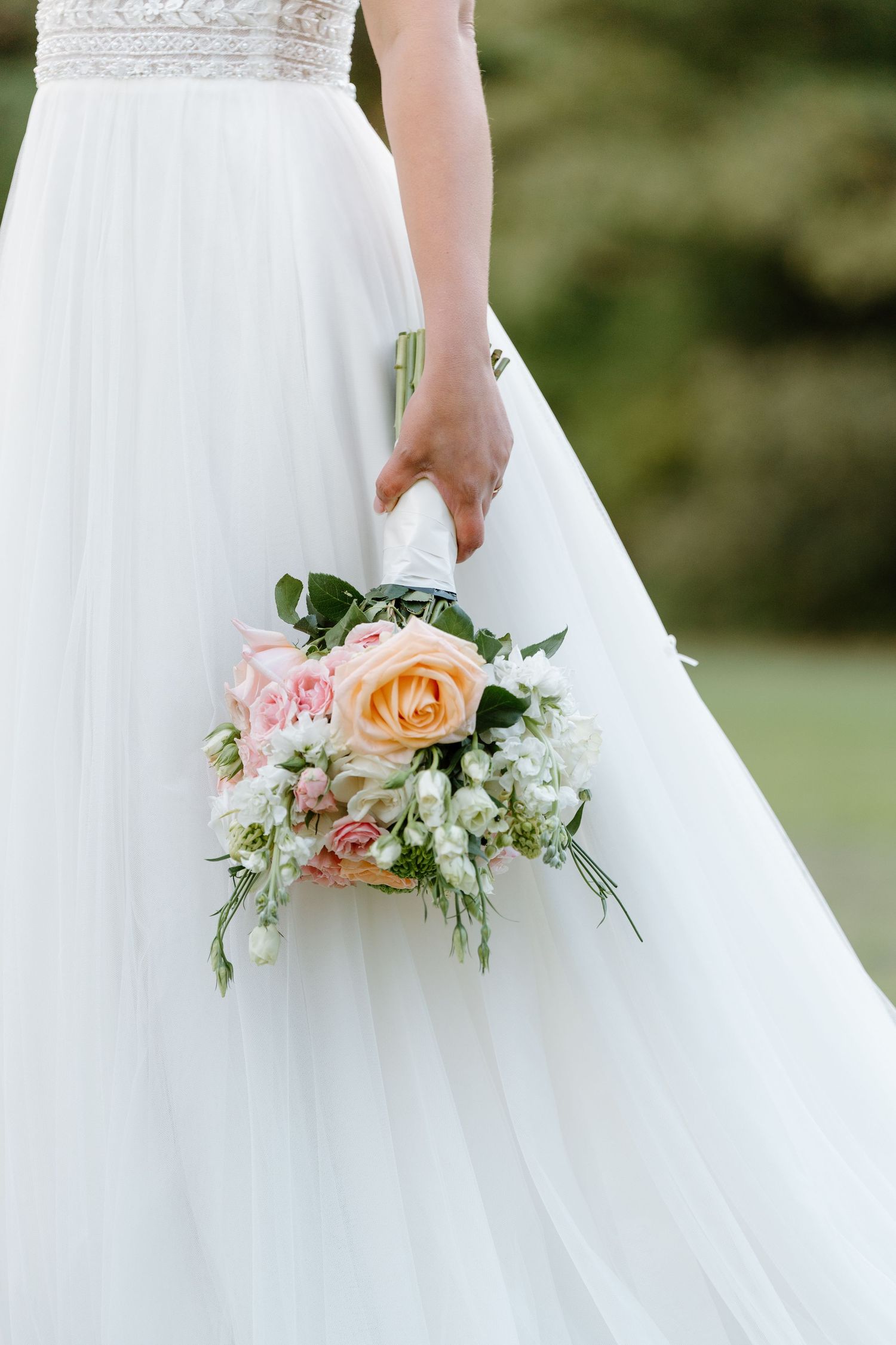 Detail of white wedding dress with delicate peach and pink floral bouquet.