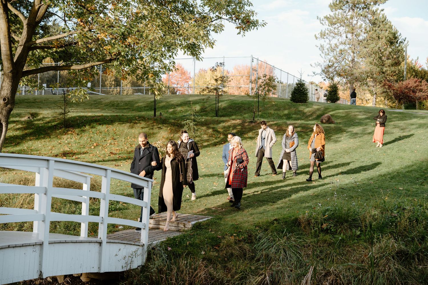Group walking across a white bridge during a fall wedding celebration.