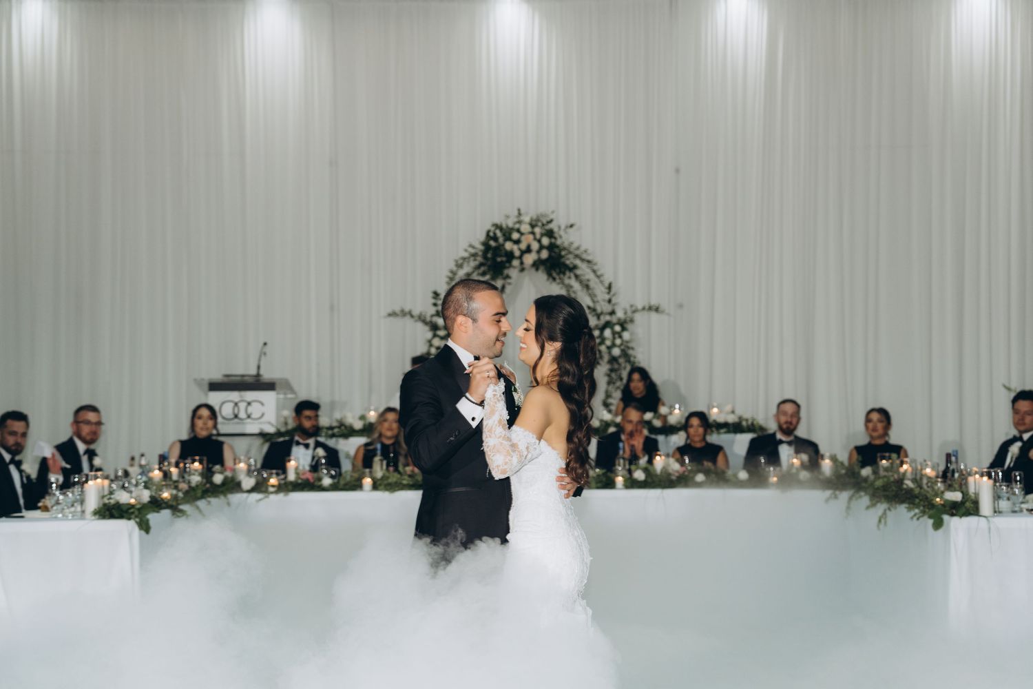 A romantic first dance between newlyweds at a wedding reception with white curtained walls and decorative lighting.