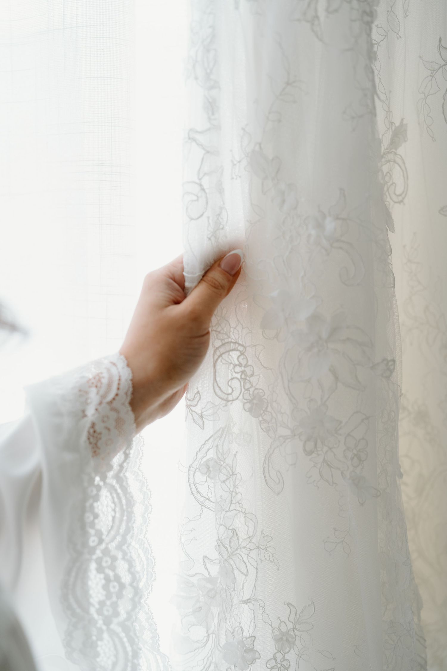 Delicate lace details on white curtains being gently touched in soft natural light.