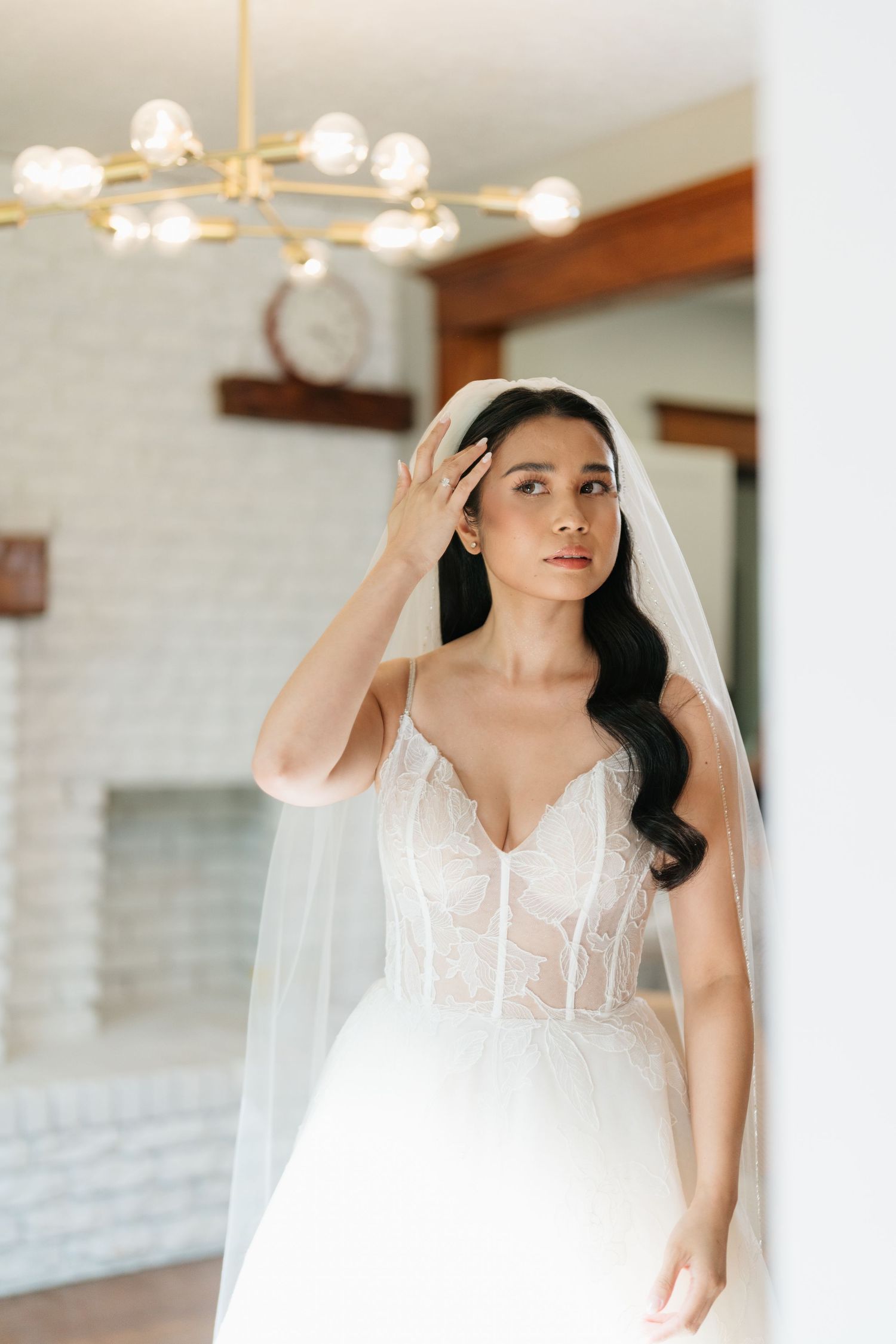 A bride in a white wedding gown with a sweetheart neckline and veil poses in an elegant indoor setting.