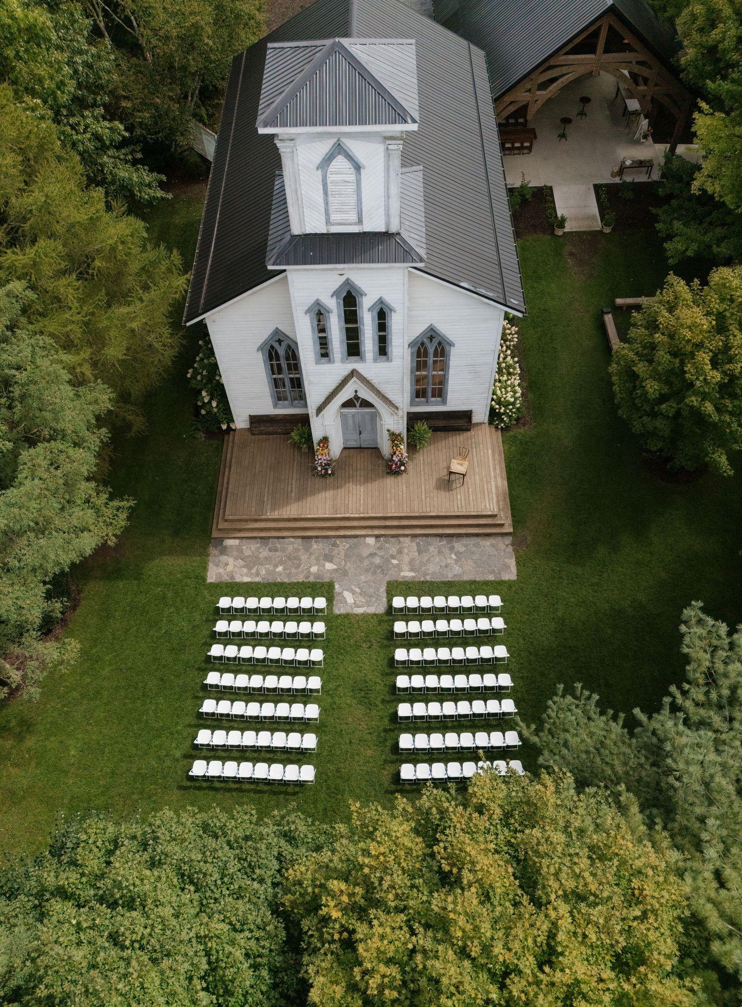 Aerial view of a white chapel with rows of white chairs set up for an outdoor wedding ceremony.